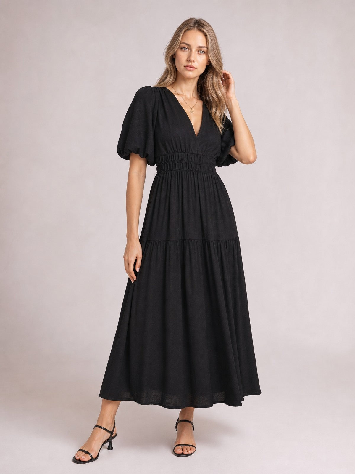 Model poses in a black elegant puff sleeve V-neck midi dress with a smocked waist, tiered flowing skirt, and feminine A-line silhouette.
