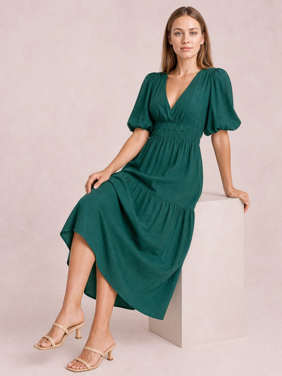A model sits in an elegant emerald green puff sleeve V-neck midi dress with a smocked waist, flowing tiered skirt, and feminine silhouette.