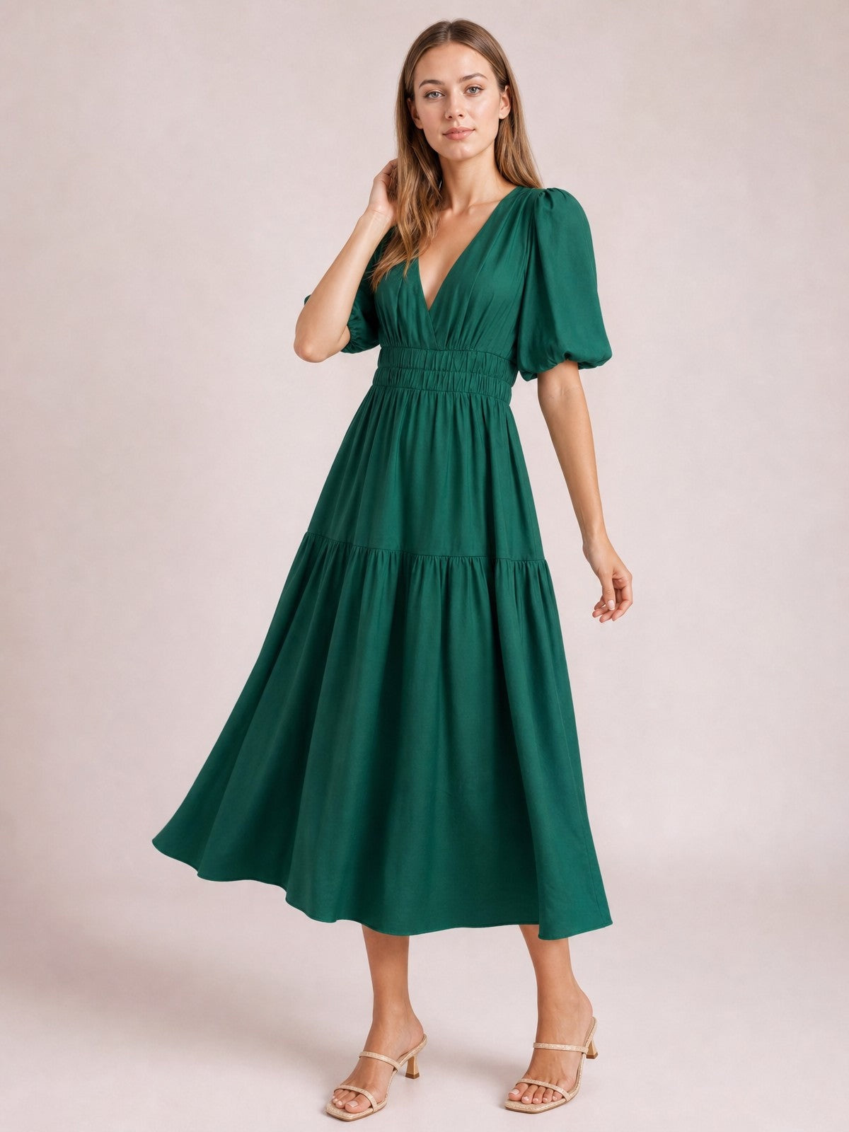 Model poses in an elegant emerald green puff sleeve V-neck midi dress with a smocked waist, tiered skirt, and flowing A-line silhouette.
