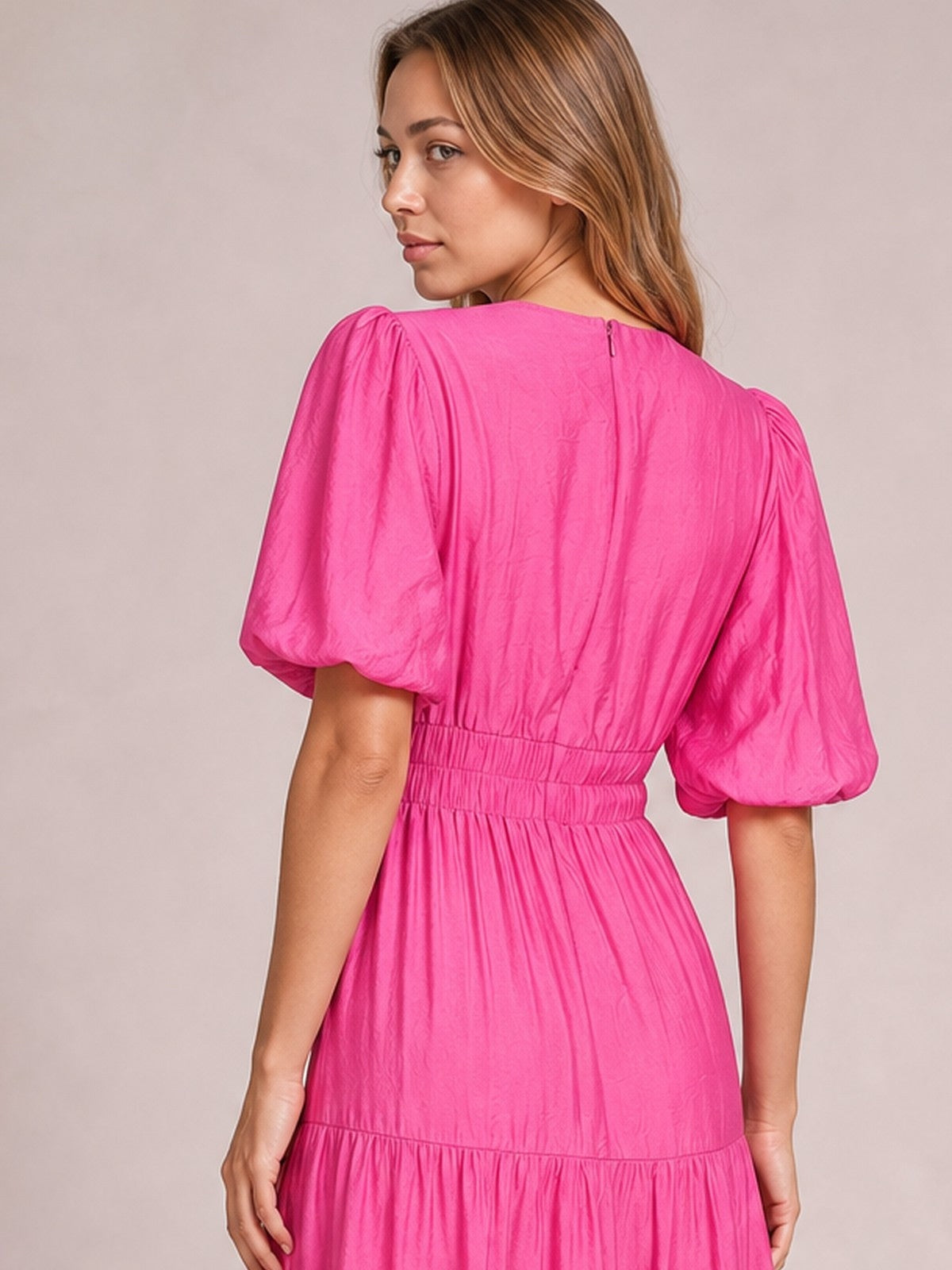 Model turns over her shoulder in a vibrant pink midi dress with voluminous puff sleeves, a smocked waist, and a flowing tiered skirt.
