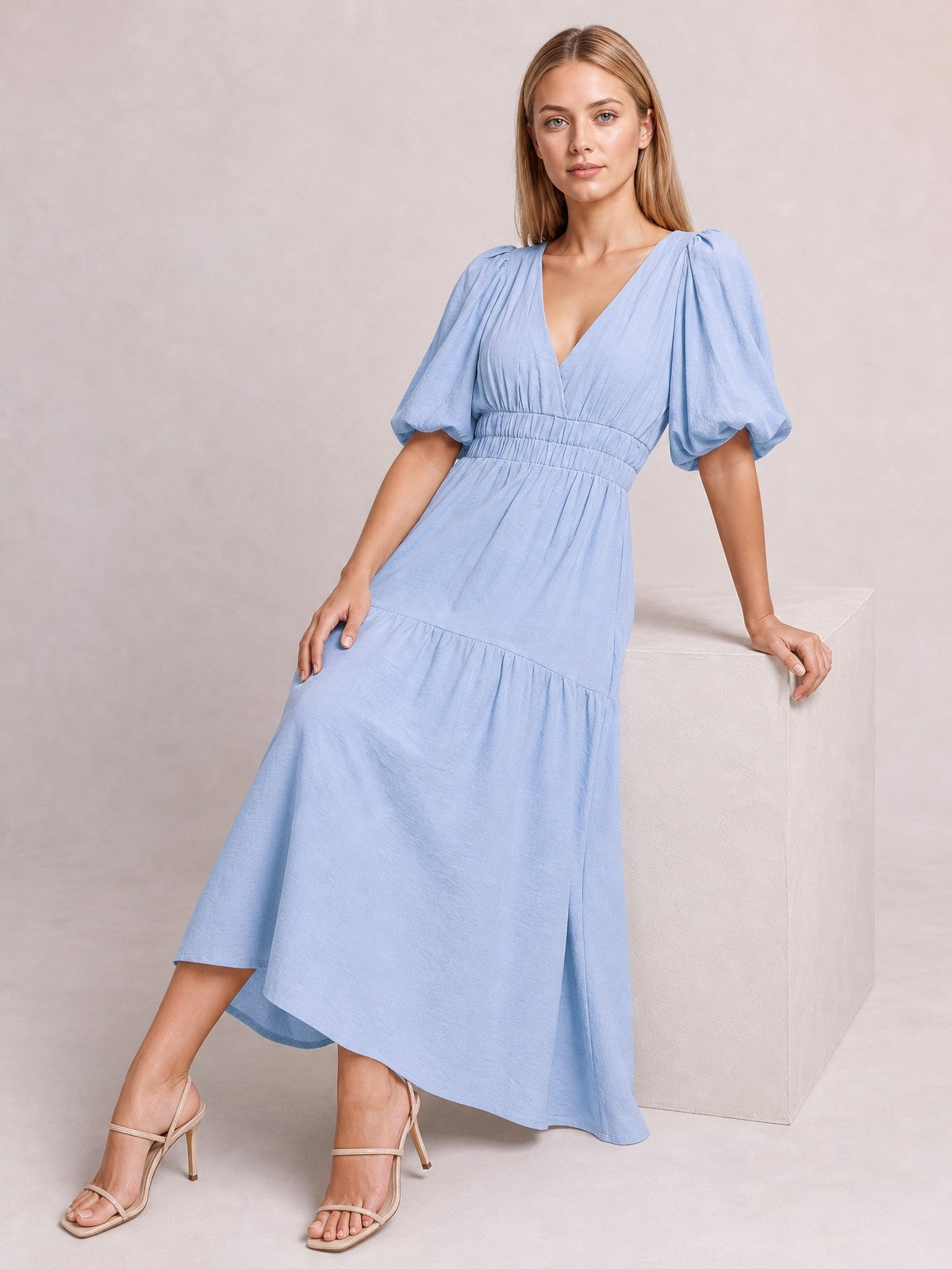 Model poses in a light blue elegant puff sleeve V-neck midi dress with a smocked waist and flowing tiered skirt.