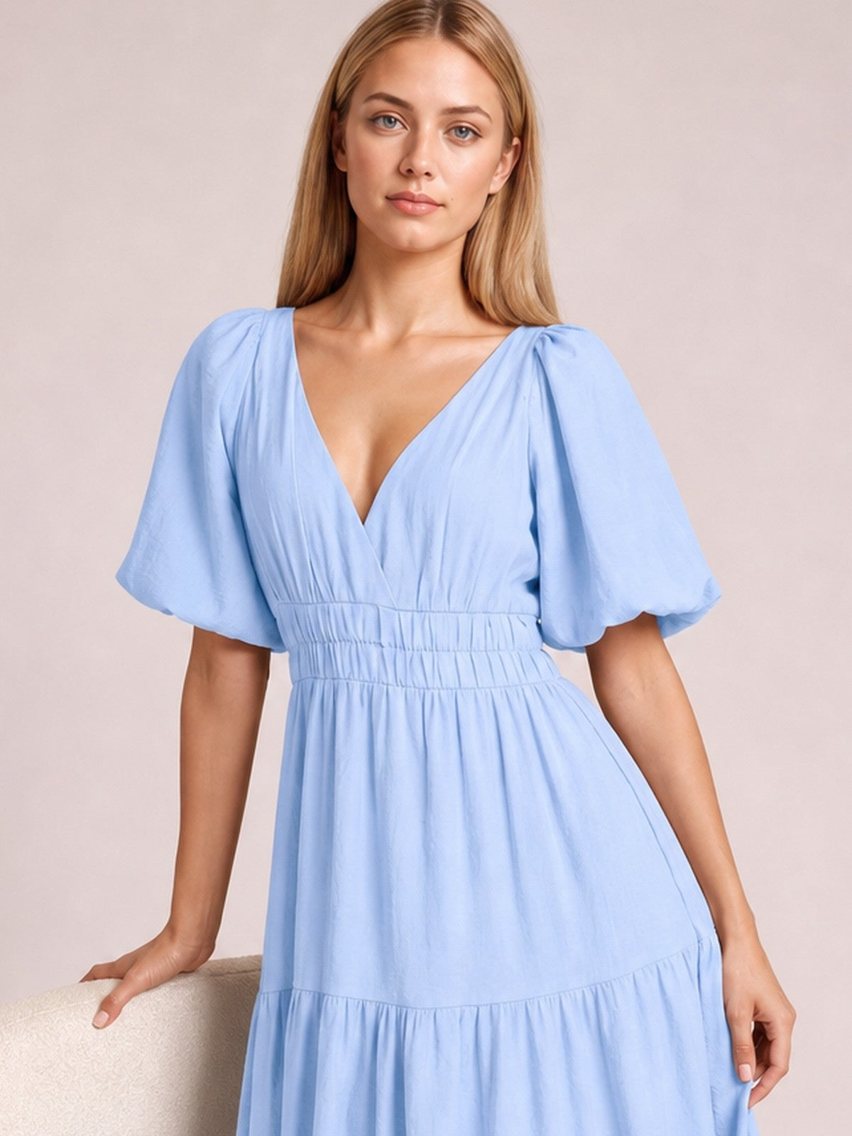 A model poses in a light blue V-neck midi dress with voluminous puff sleeves, a smocked waist, and a flowing tiered skirt.