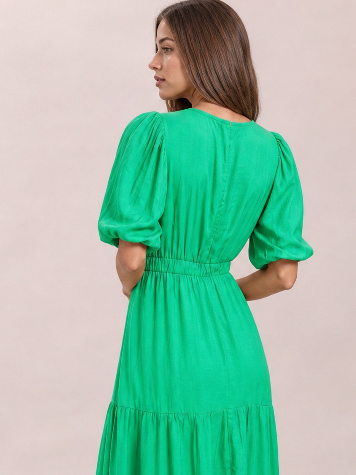 A model poses with her back to the camera in a bright green midi dress featuring puff sleeves, a smocked waist, and a flowing tiered skirt.