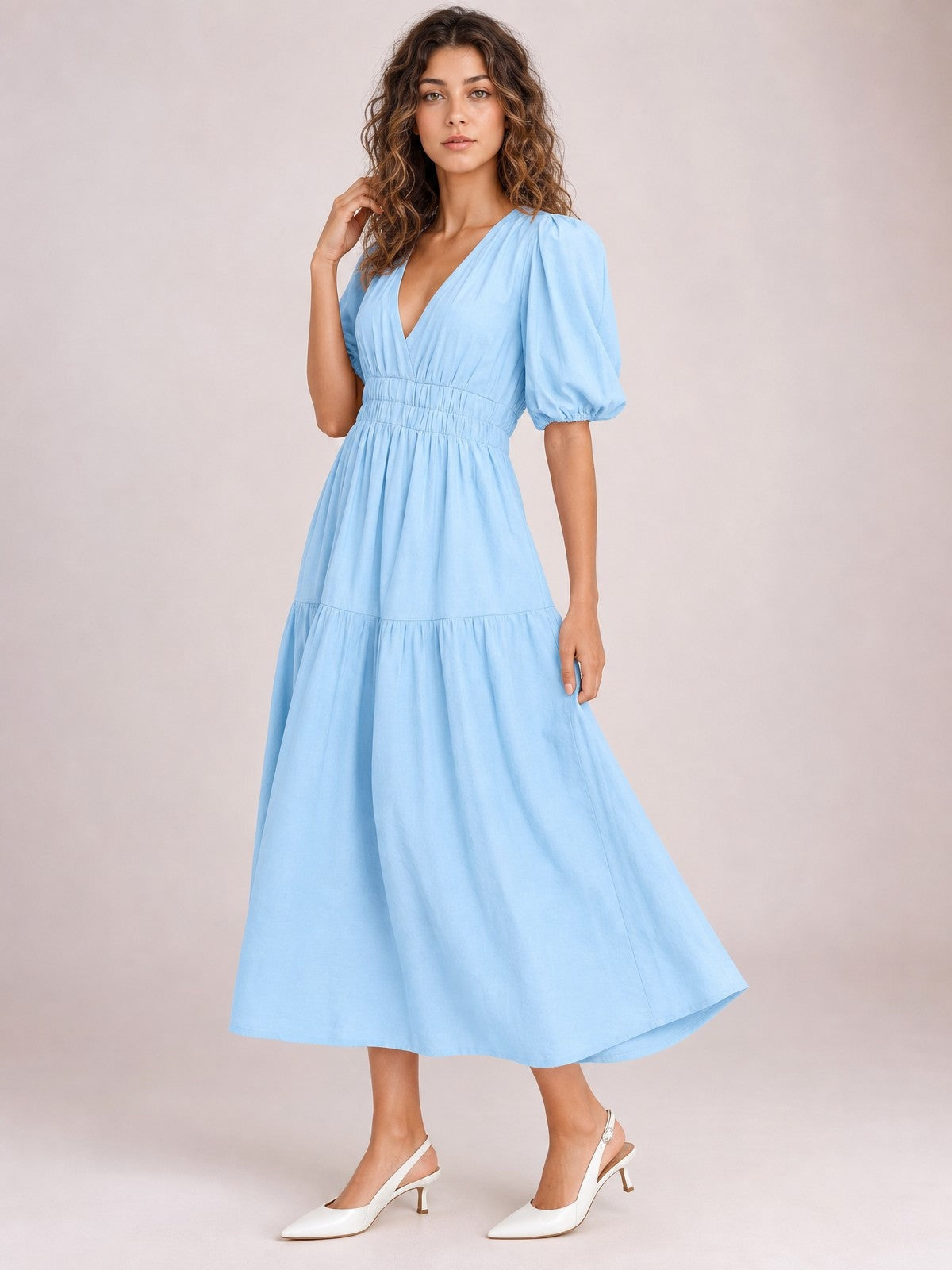Model poses in a light blue V-neck midi dress with gathered puff sleeves, a smocked waist, and a flowing tiered skirt.