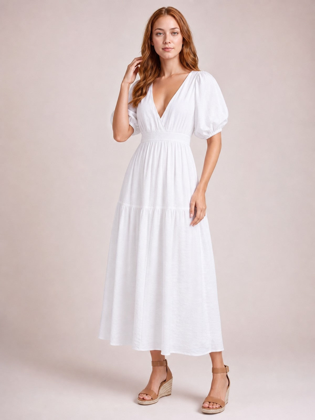 Model poses in a white elegant midi dress with a V-neck, puff sleeves, smocked waist, tiered skirt, and flowing A-line silhouette.