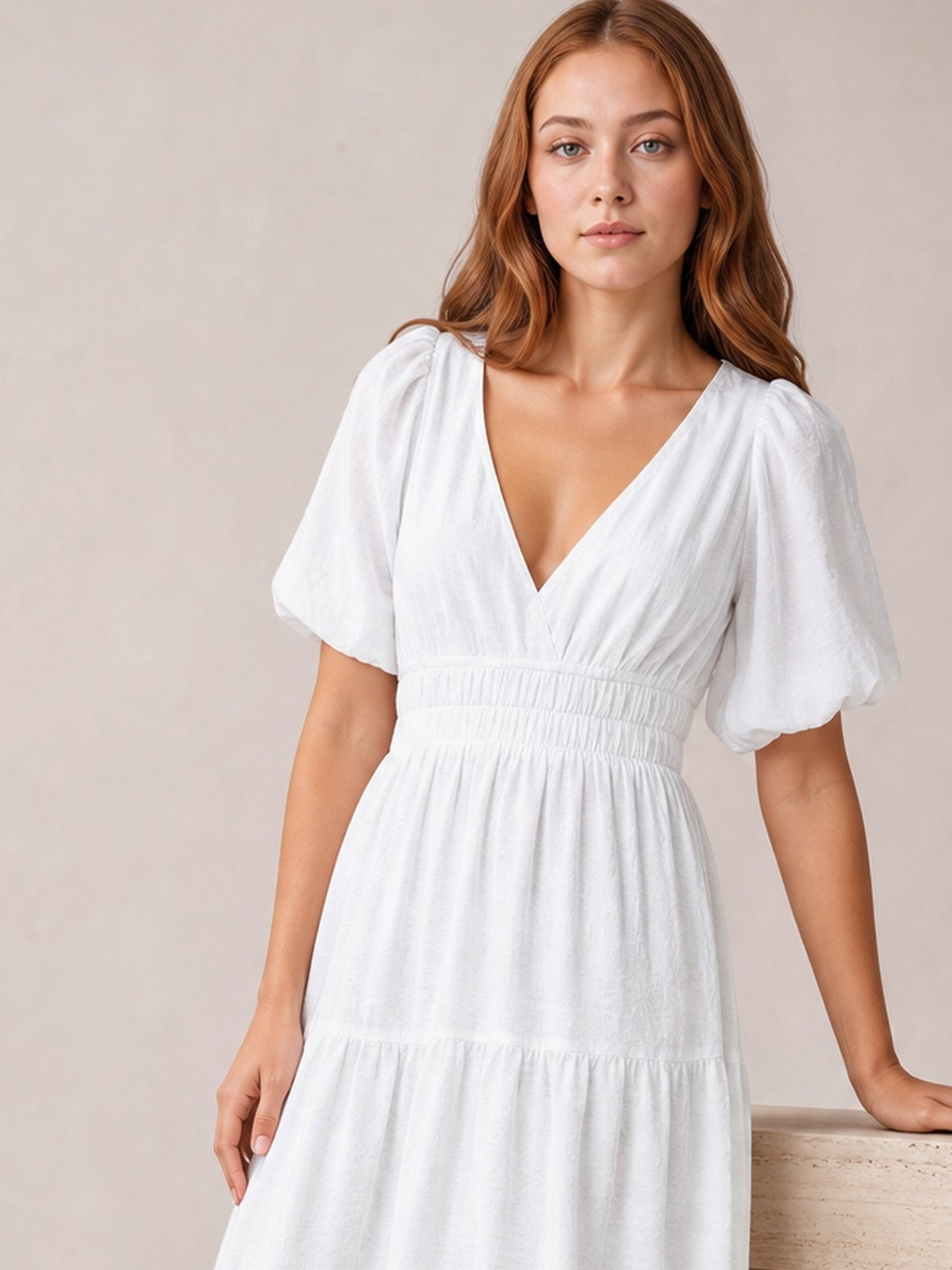 A model poses in a white elegant puff sleeve V-neck midi dress with a smocked waist and tiered skirt, one hand resting at her side.