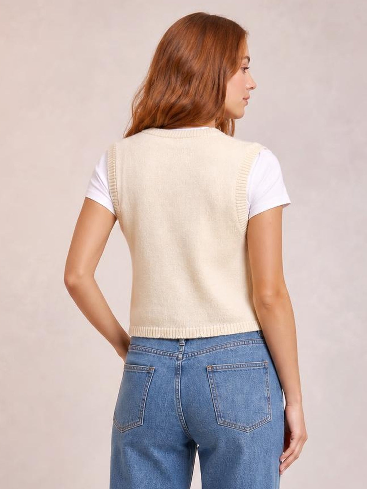 Model shown from the back wears a cream embroidered sweater vest over a white tee, with ribbed armholes and hem in a relaxed straight silhouette.