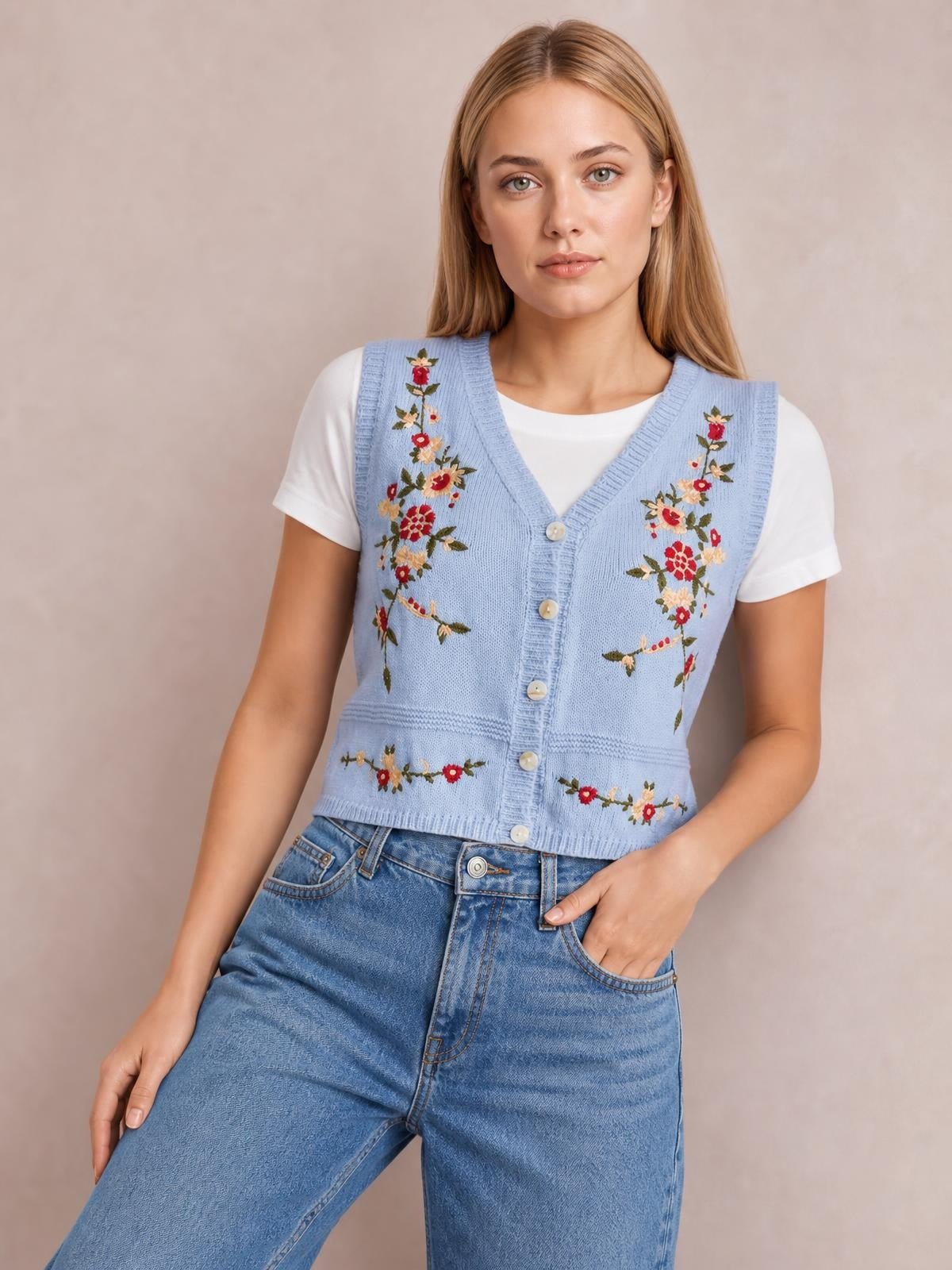 Model wearing a light blue embroidered button-up sweater vest with a V-neck, ribbed trim, fitted silhouette, and floral detailing over a white T-shirt.