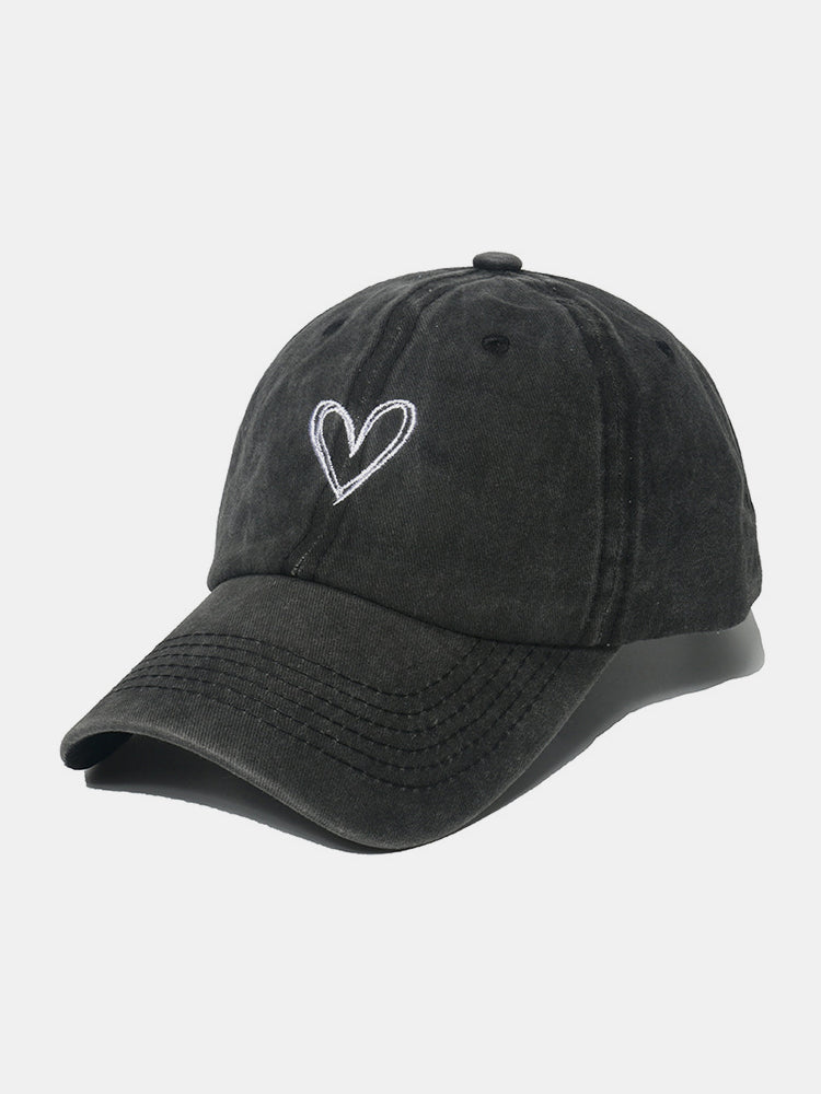 Black washed cotton baseball cap with a relaxed six-panel silhouette, curved brim, tonal stitching, and a white embroidered heart motif.