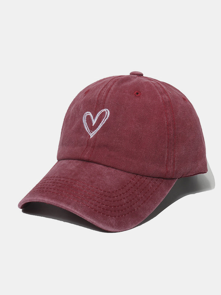A burgundy washed cotton baseball cap with a six-panel crown, curved brim, tonal stitching, and a contrasting embroidered heart motif at the front.