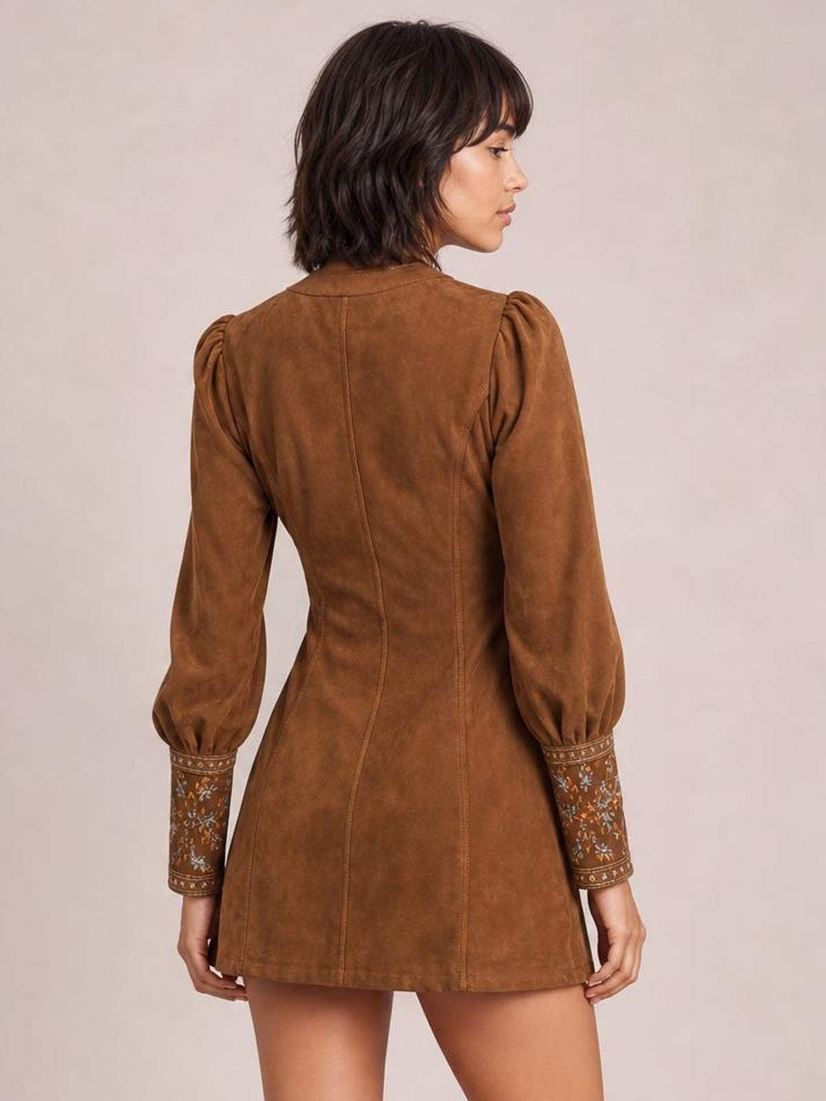 Back view of a model in a brown embroidered mini dress with lantern sleeves, floral-patterned cuffs, a fitted seamed bodice, and flared hem.