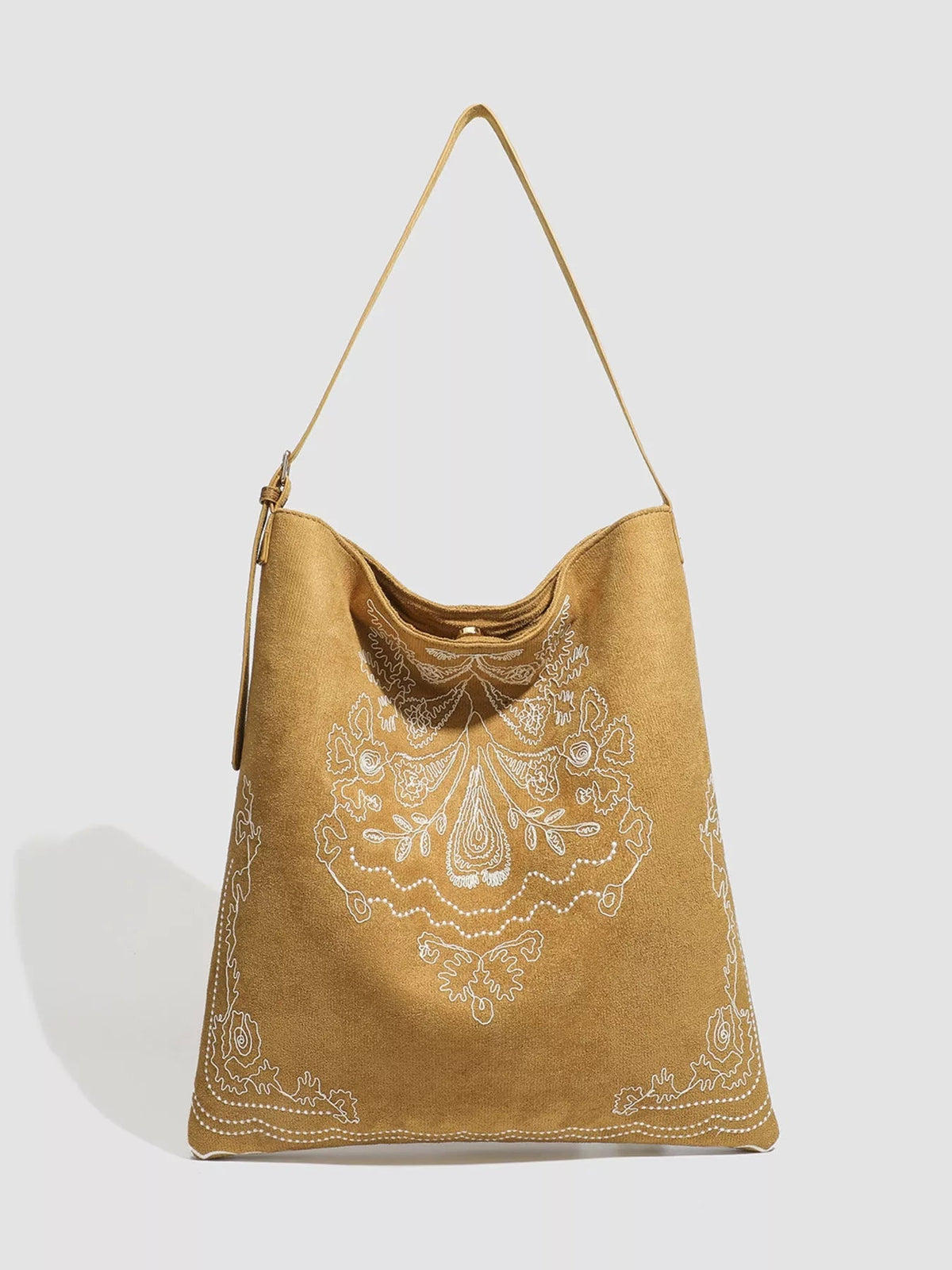 Large tan suede handbag with a slouchy shoulder silhouette, long slender strap, curved opening, and ornate white floral embroidery across the front.