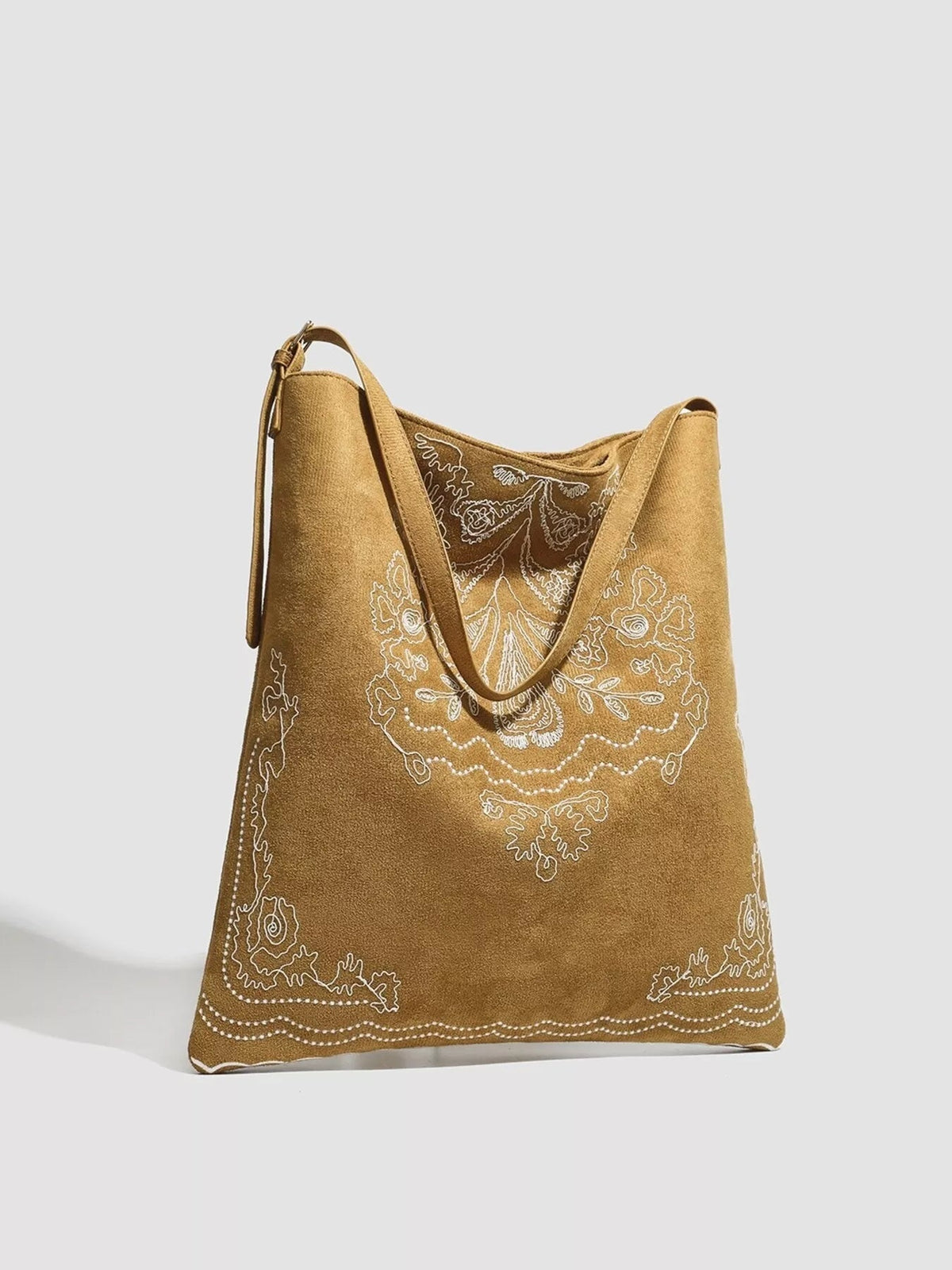 Large tan suede handbag with a soft tote silhouette, long shoulder straps, and intricate white floral embroidery across the front and lower edges.
