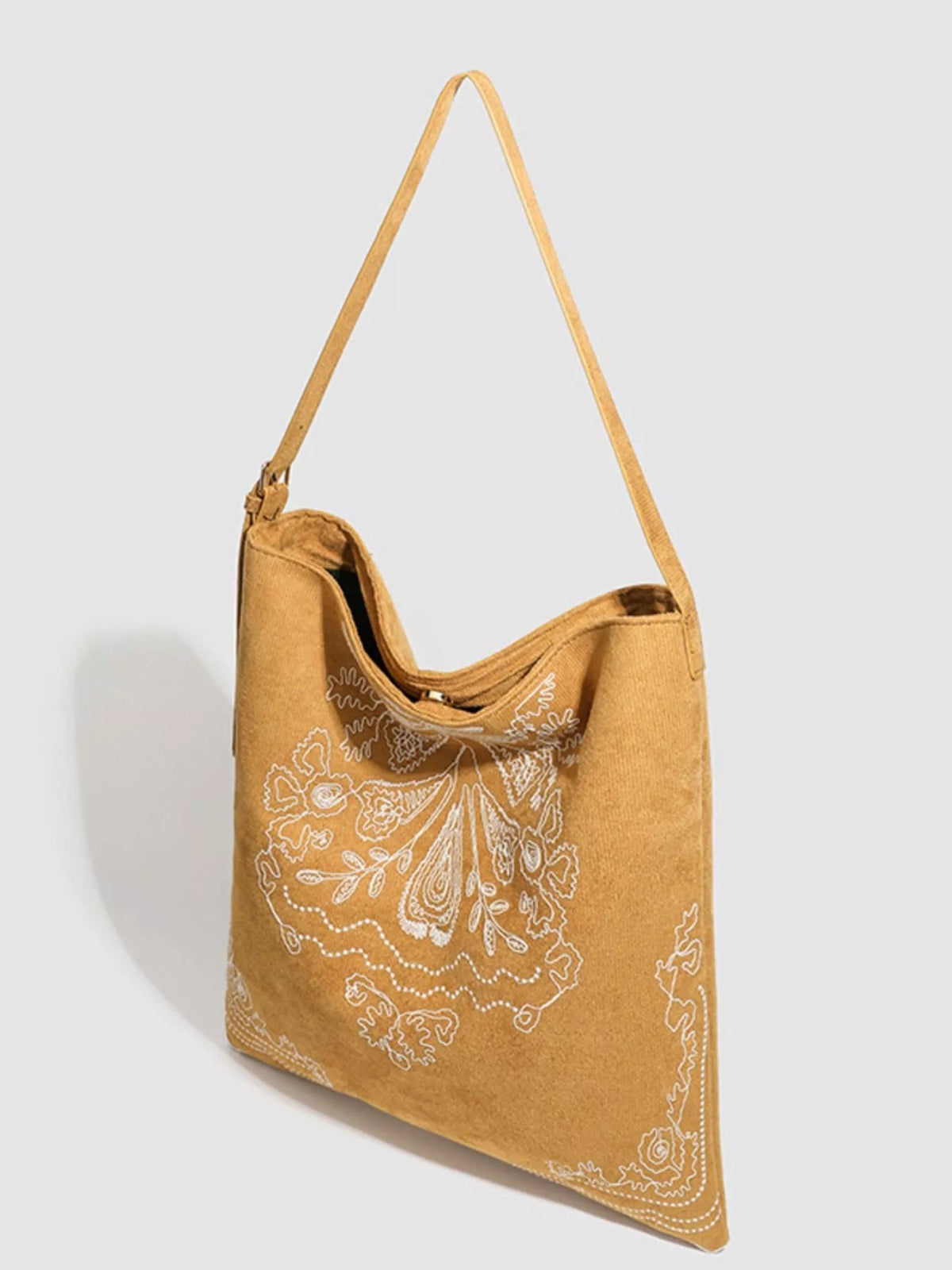 Large tan suede handbag with a soft slouchy silhouette, long shoulder strap, open top, and intricate white embroidered floral and paisley detailing.
