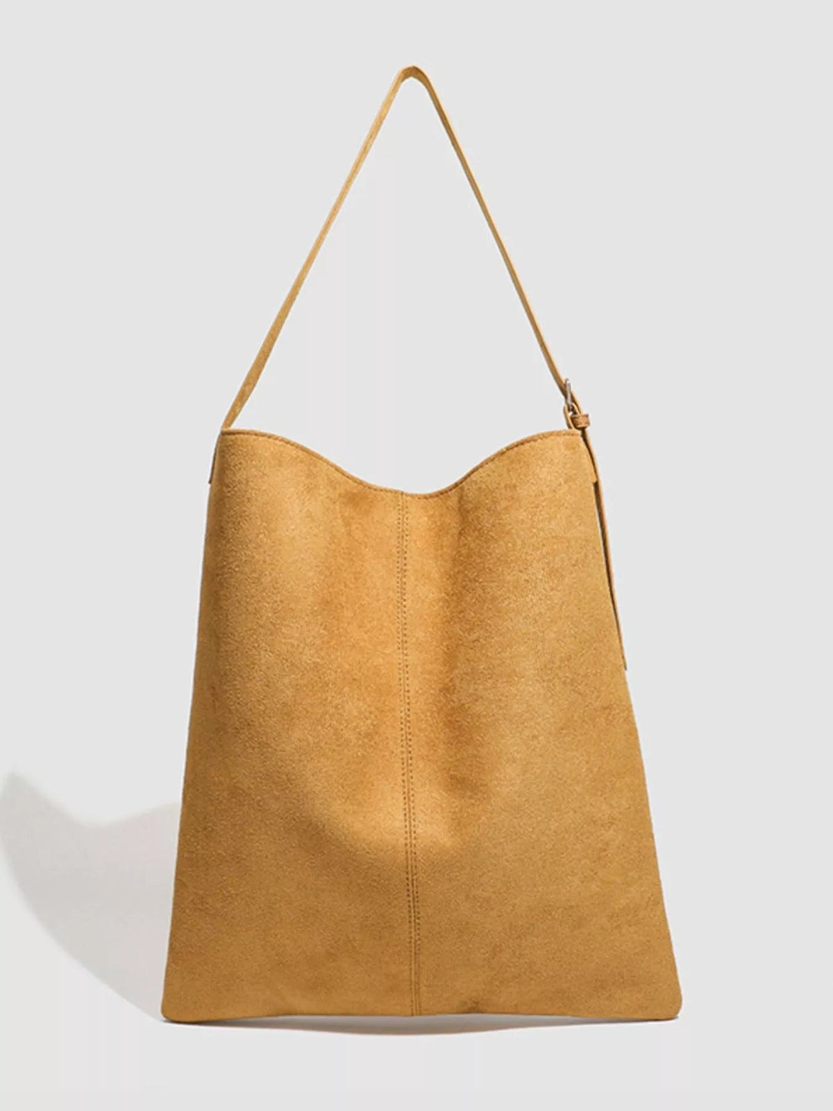 Large tan suede handbag with a slouchy trapezoid silhouette, curved top edge, long shoulder strap, adjustable buckle, and centered vertical stitching.