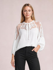 Model wearing a white embroidered tie-neck blouse with a collared neckline, sheer mesh raglan sleeves, and voluminous puff cuffs.