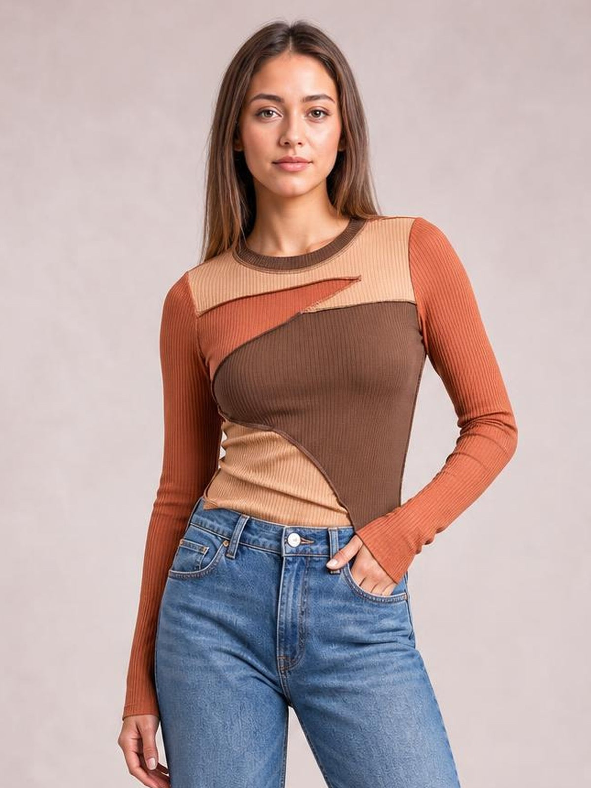 Model in jeans wears a fitted long-sleeve round-neck T-shirt with exposed contrast seams and color-blocked brown, rust, and beige ribbed panels.