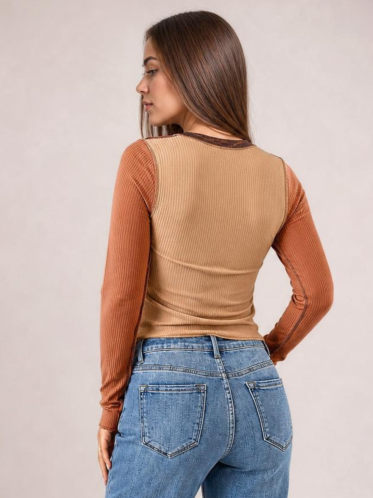Model shown from behind wears a fitted tan long-sleeve T-shirt with rust contrast sleeves, a round neck, ribbed texture, and exposed seams.