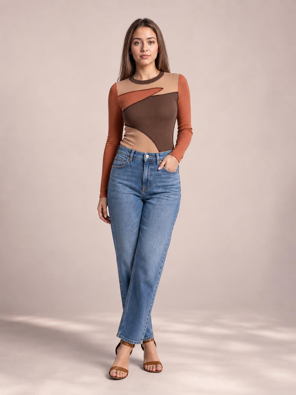 A model stands with one hand in her jeans pocket, wearing a fitted color-block long-sleeve T-shirt with a round neck and exposed contrast seams.