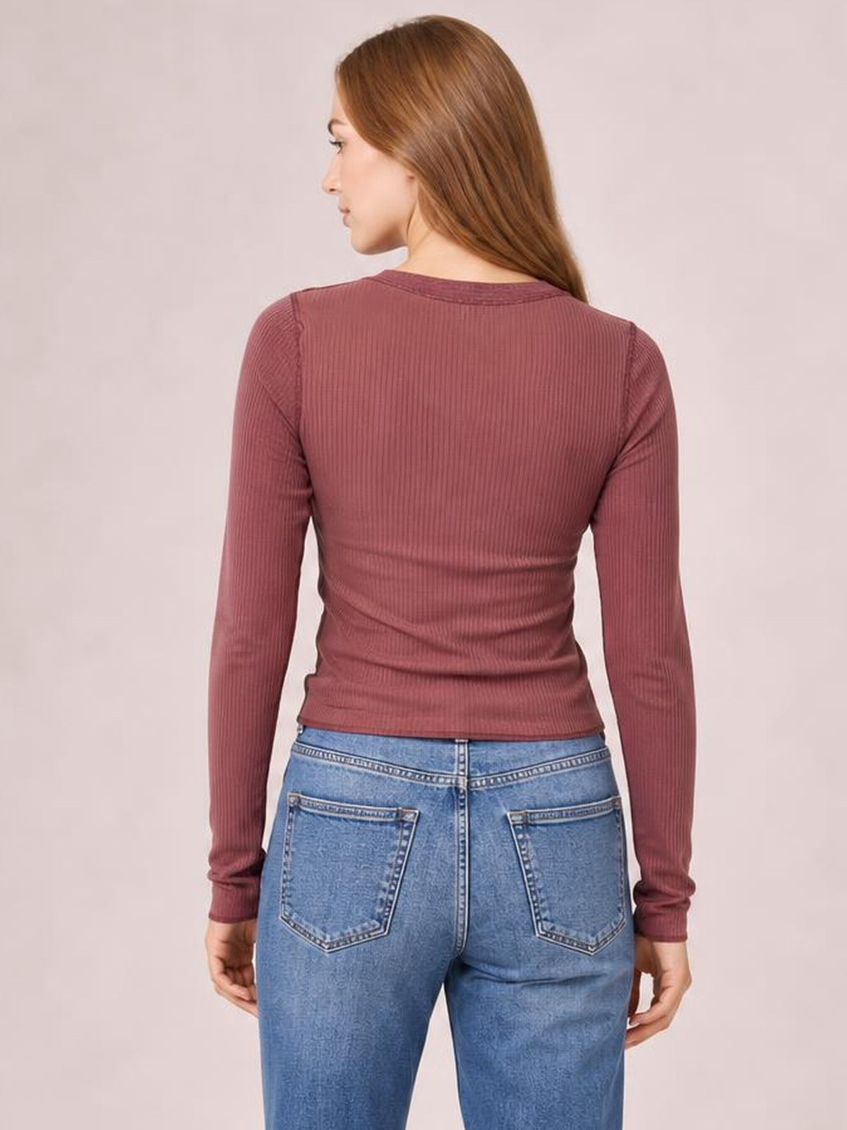 A model shown from behind wears a burgundy exposed-seam contrast round-neck long-sleeve T-shirt with a fitted, slightly stretchy silhouette.
