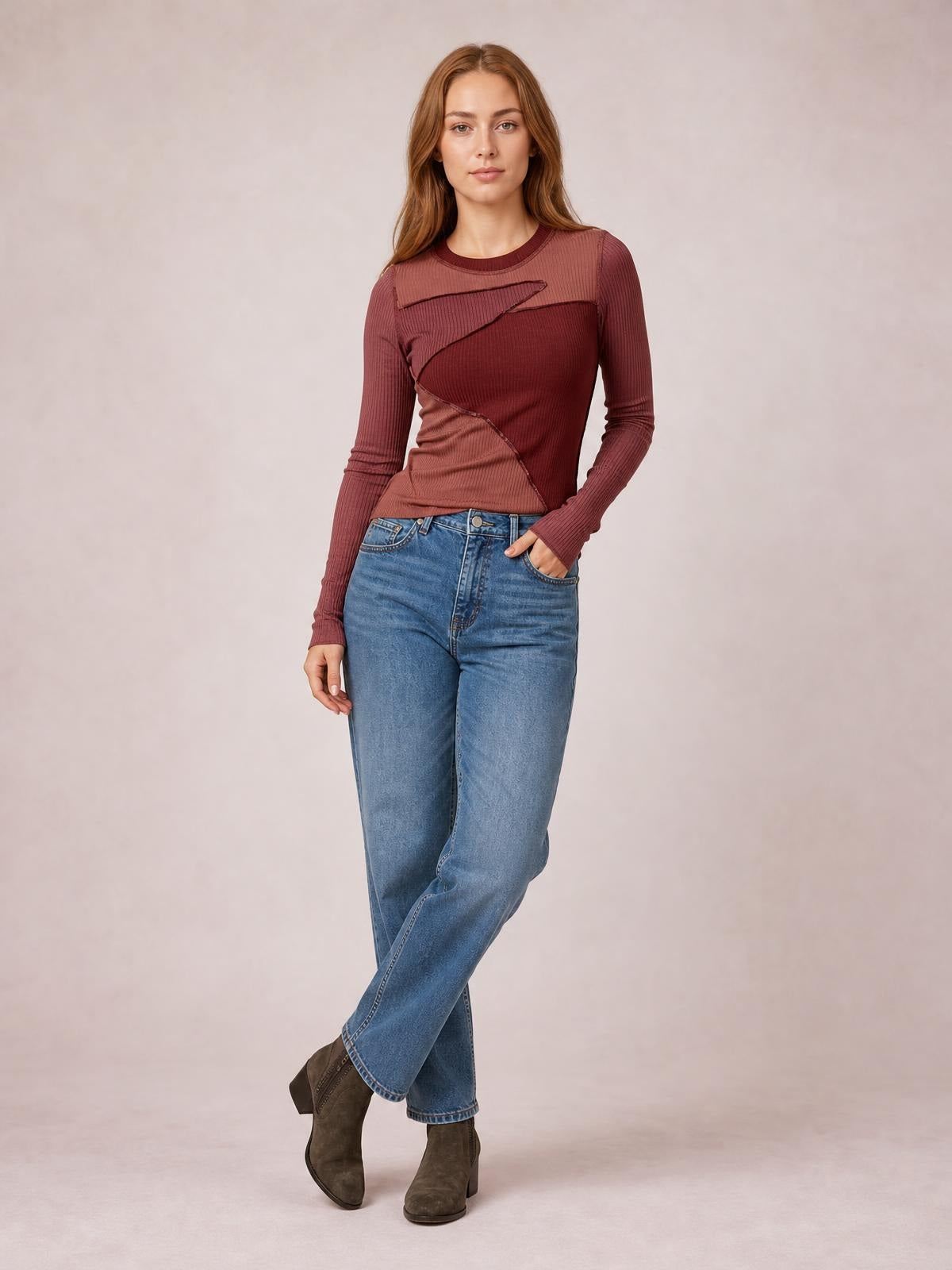 Model poses with one hand in her pocket wearing a fitted burgundy long-sleeve t-shirt with a round neck, contrast panels, and exposed seams.