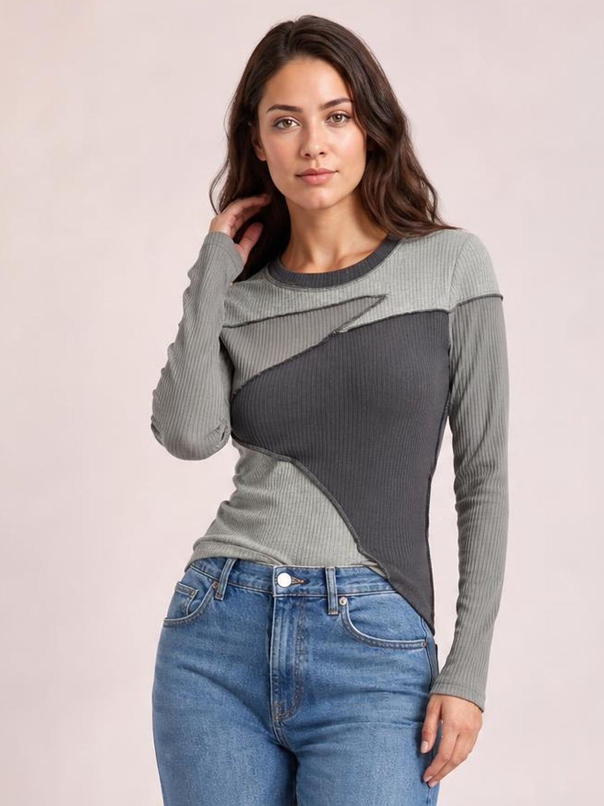 Model poses in a fitted gray and charcoal contrast long-sleeve T-shirt with a round neck, exposed seams, ribbed texture, and curved color-block panels.