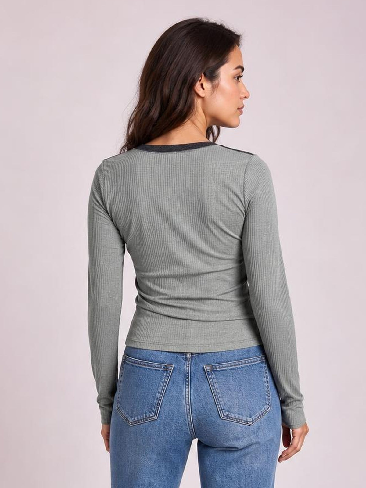 Model shown from the back in a gray fitted long-sleeve T-shirt with a contrast round neck and exposed seams, posing in blue jeans.