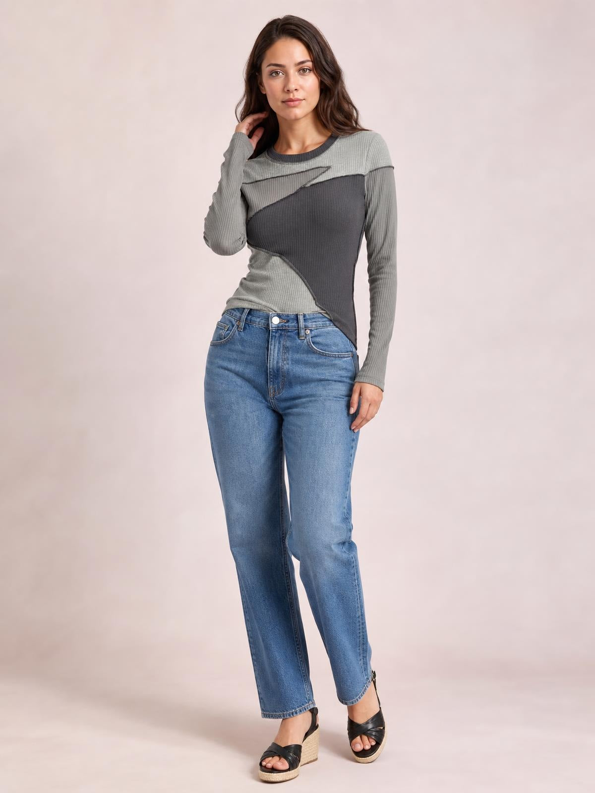 A model poses in a fitted gray contrast long-sleeve T-shirt with a round neck, exposed seams, and angular color-blocked panels.