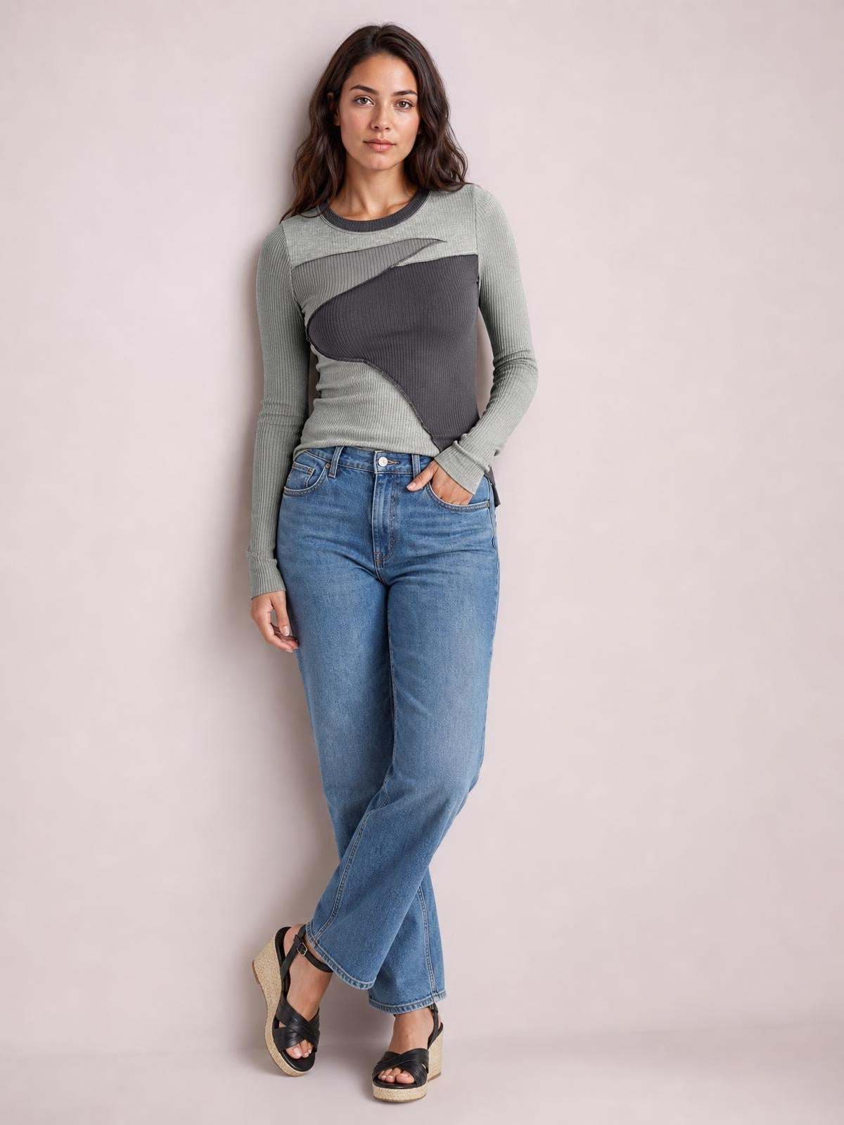 Model wearing a fitted gray contrast round neck long sleeve T-shirt with exposed seams and a paneled silhouette, standing with one hand in her jeans pocket.
