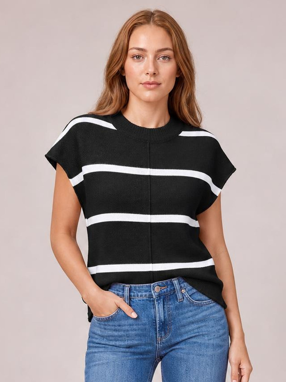 Model wears a black knit top with white contrast stripes, round neck, exposed center seam, short sleeves, and a relaxed silhouette, posing with one hand in her jeans pocket.