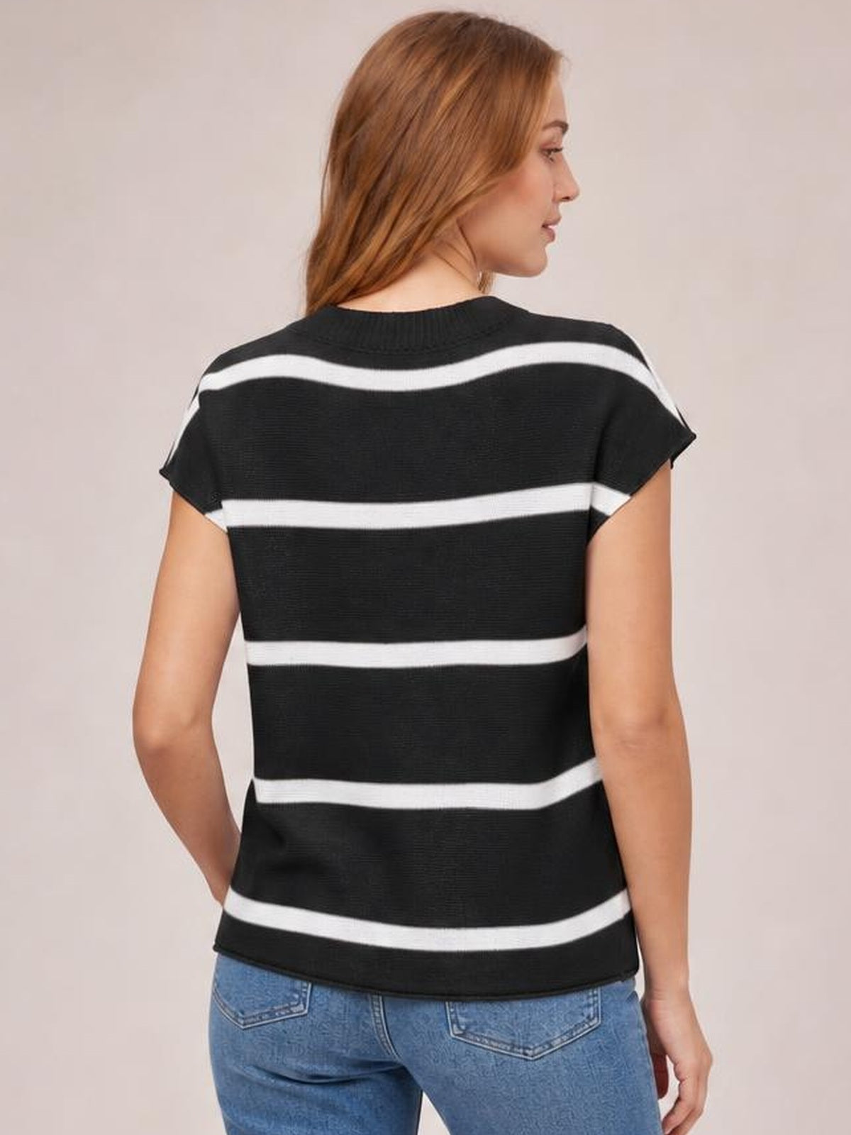 Model shown from the back in a black knit top with contrasting white horizontal stripes, round neck, exposed seam details, short sleeves, and a relaxed silhouette.
