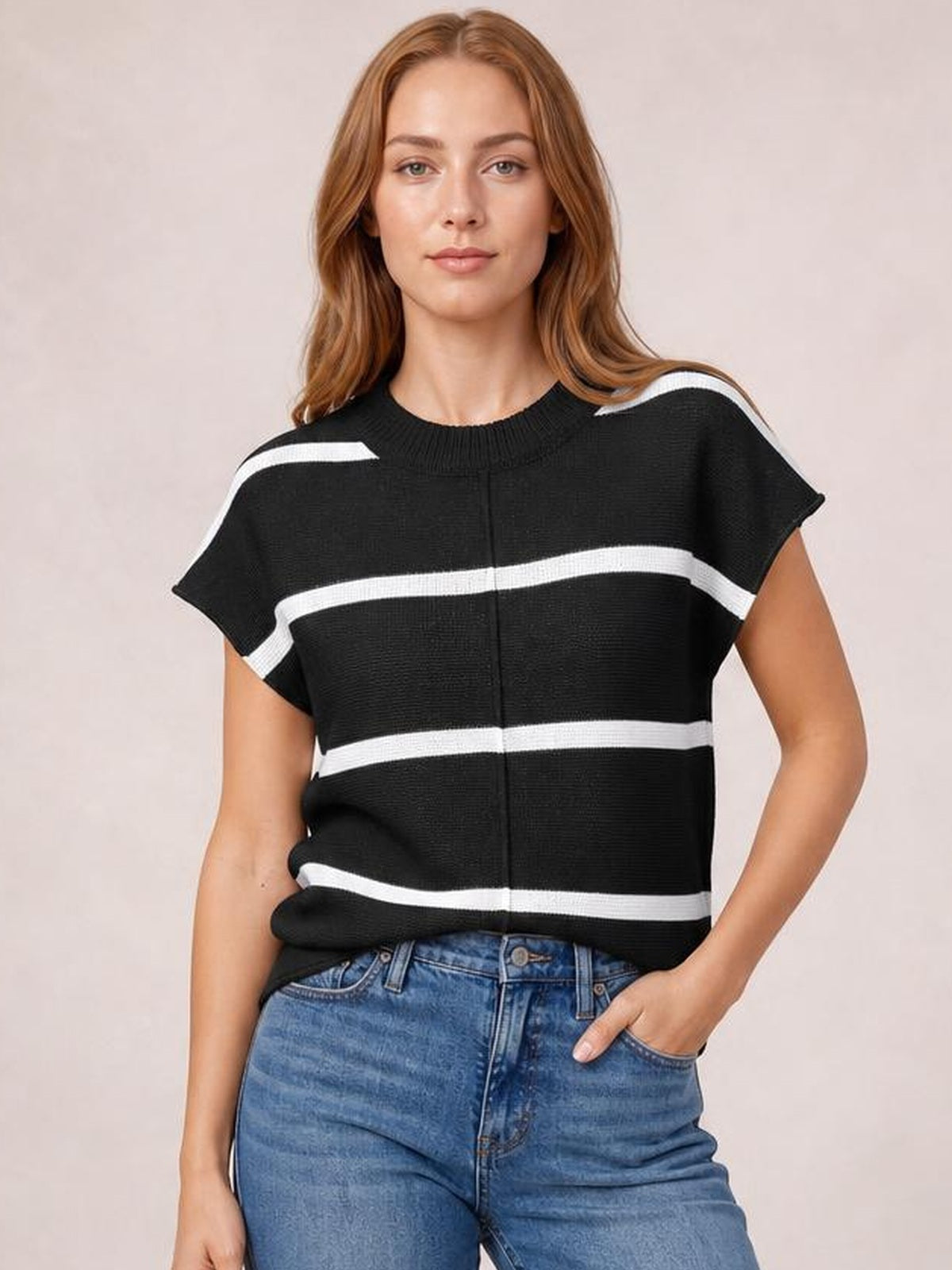 A model wears a black knit top with white contrast stripes, a round neck, short sleeves, exposed center seam, and relaxed silhouette while posing with one hand in her jeans pocket.