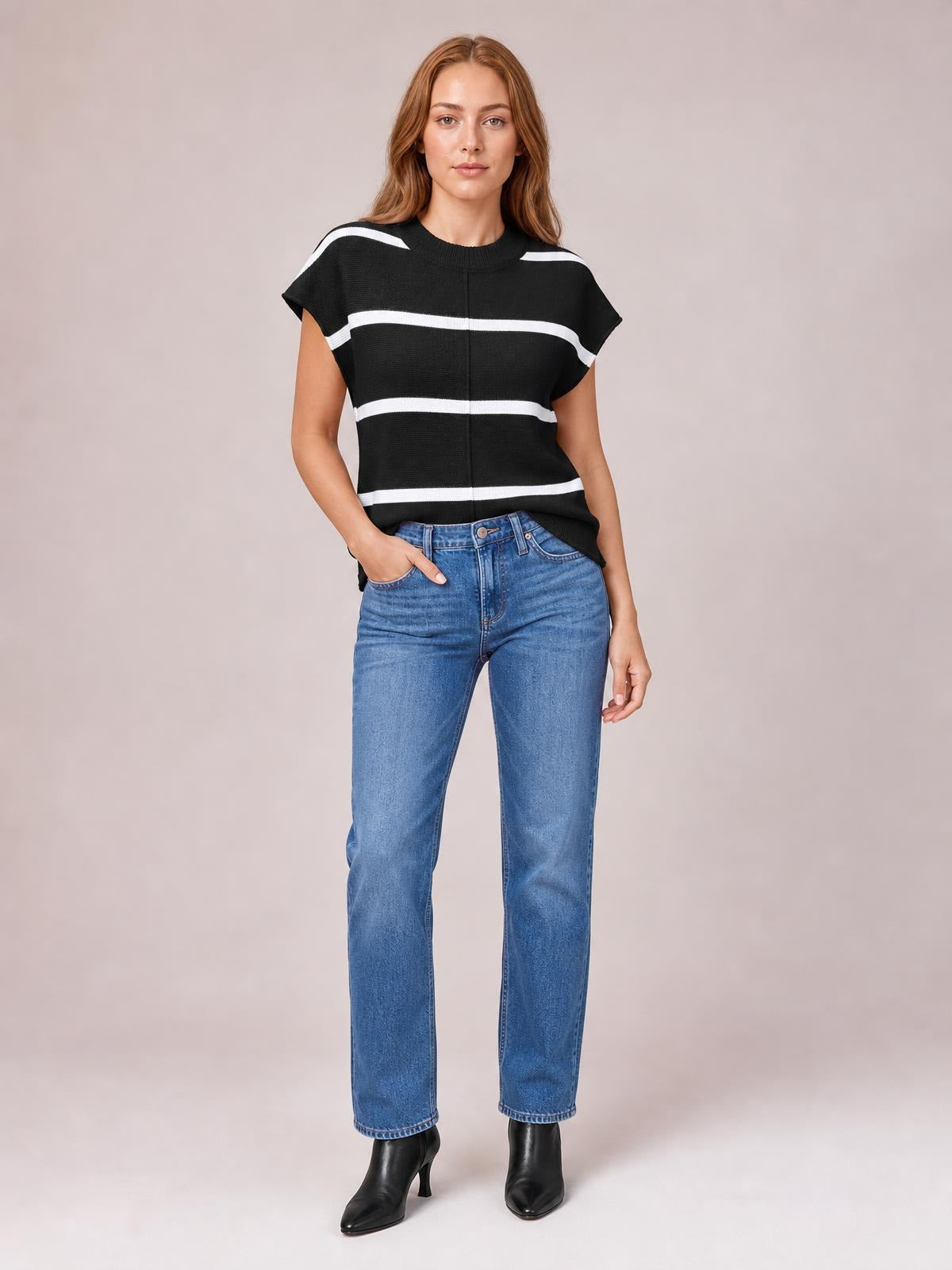 Model wears a black contrast-striped knit top with a round neck, exposed center seam, short sleeves, and a relaxed silhouette, standing with one hand in her jeans pocket.