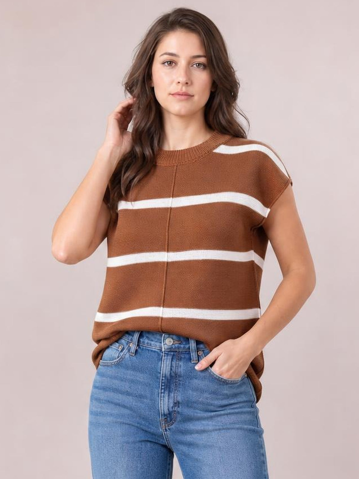Model wearing a brown contrast striped round-neck knit top with exposed center seam, short sleeves, and a relaxed silhouette, posing with one hand in her jeans pocket.