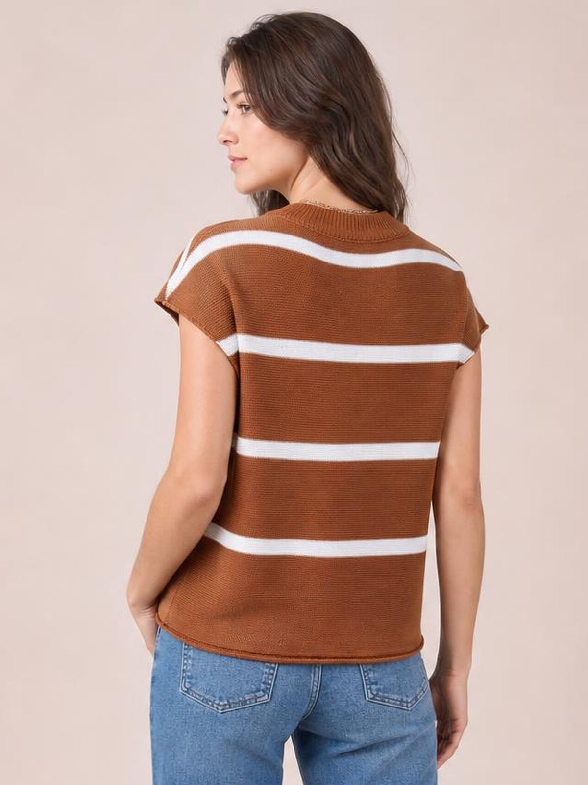 A woman stands with one hand at her hip, modeling a rust-brown knit top with a round neck, short sleeves, exposed seams, and white contrast stripes.