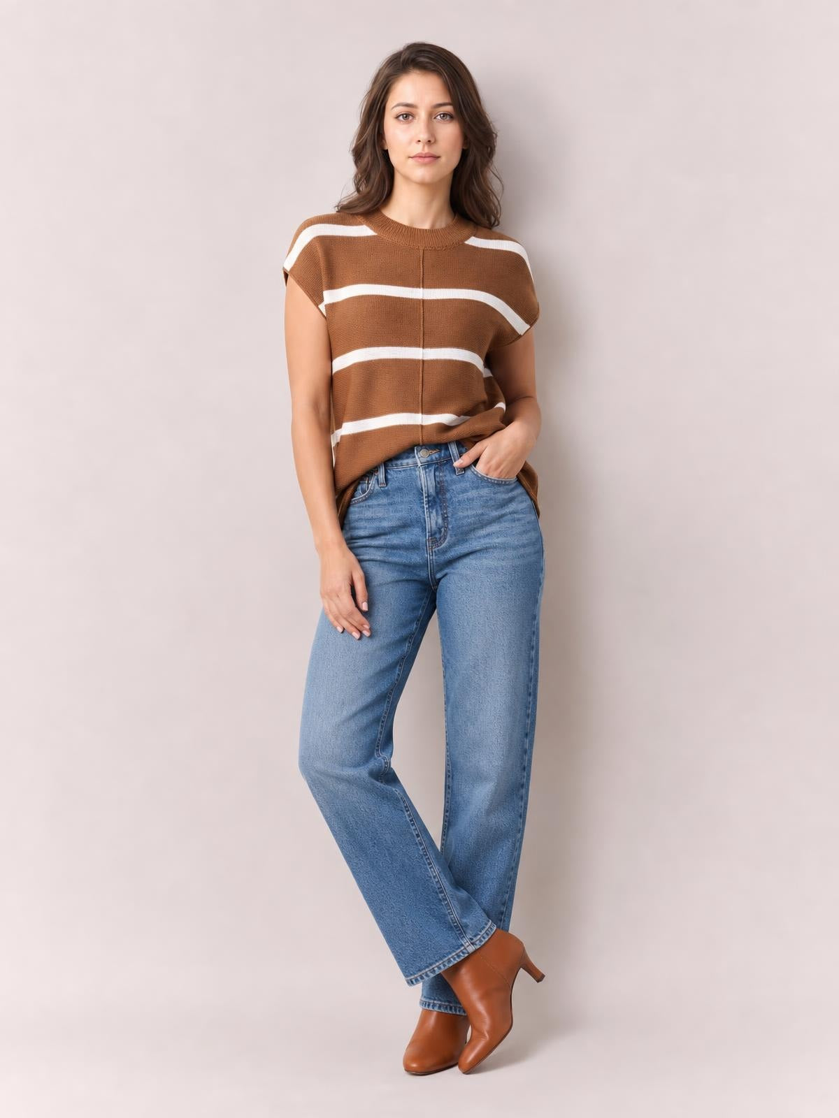 A model poses with one hand in her pocket wearing a brown knit top with white contrast stripes, a round neck, exposed center seam, and relaxed silhouette.