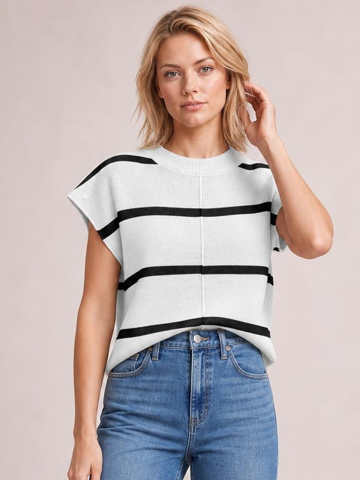 A woman poses with one hand touching her hair, wearing a relaxed white knit top with black contrast stripes, a round neck, short sleeves, and exposed center seam.