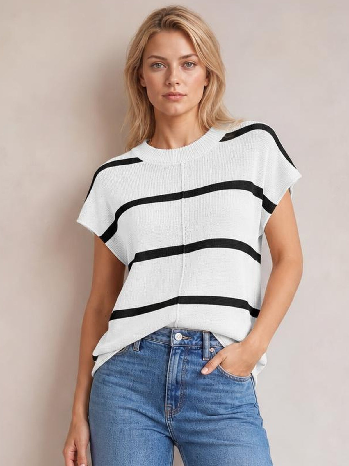 Model wearing a white contrast striped round neck knit top with exposed center seam, short sleeves, and a relaxed silhouette, posing with one hand in her jeans pocket.