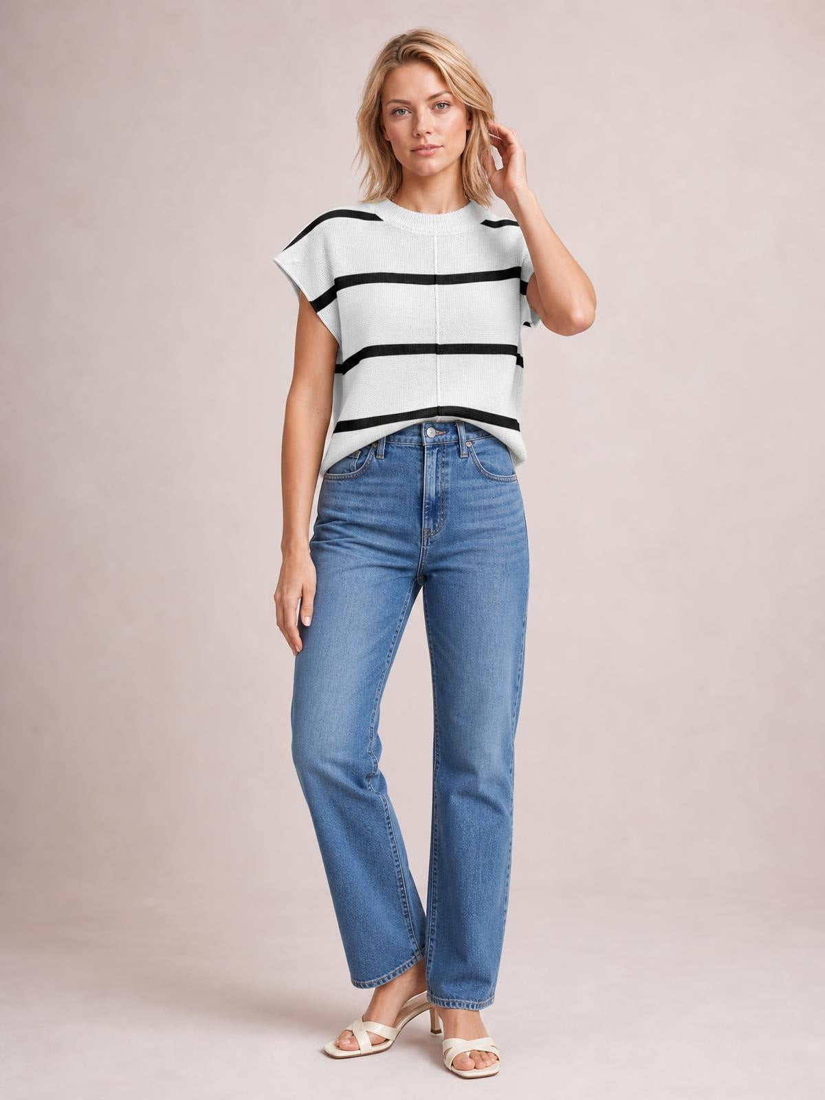 A model wears a white knit top with black contrast stripes, round neck, exposed center seam, cap sleeves, and a relaxed boxy silhouette while touching her hair.
