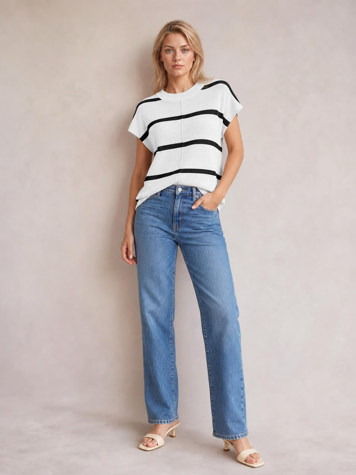 A woman stands in a white knit top with black contrast stripes, round neck, exposed center seam, short sleeves, and a relaxed boxy silhouette.