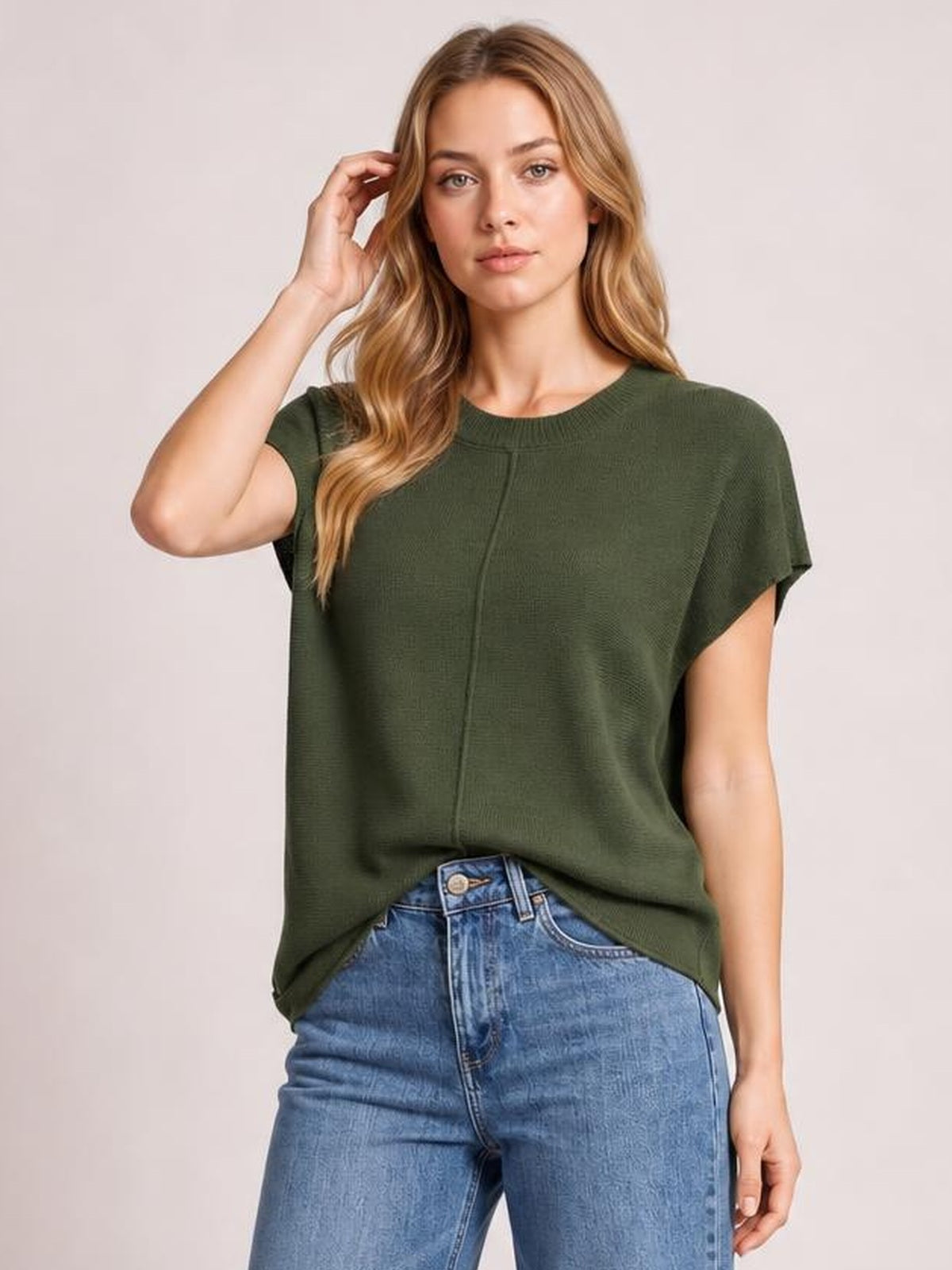 A model poses in a dark olive exposed seam sweater with a round neck, short sleeves, relaxed loose silhouette, and visible center-front construction seam.