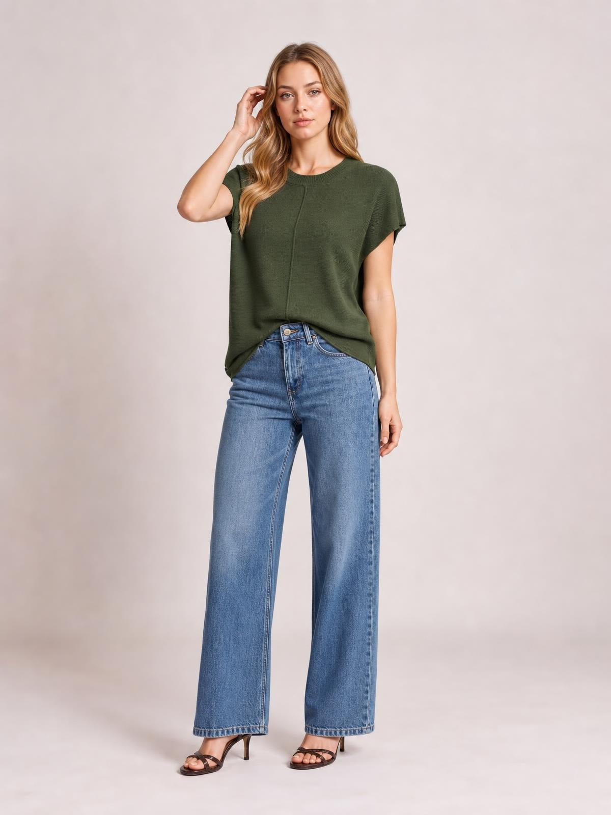 A model poses with one hand in her hair wearing an olive green, relaxed-fit sweater with a round neck, short sleeves, and an exposed center seam.