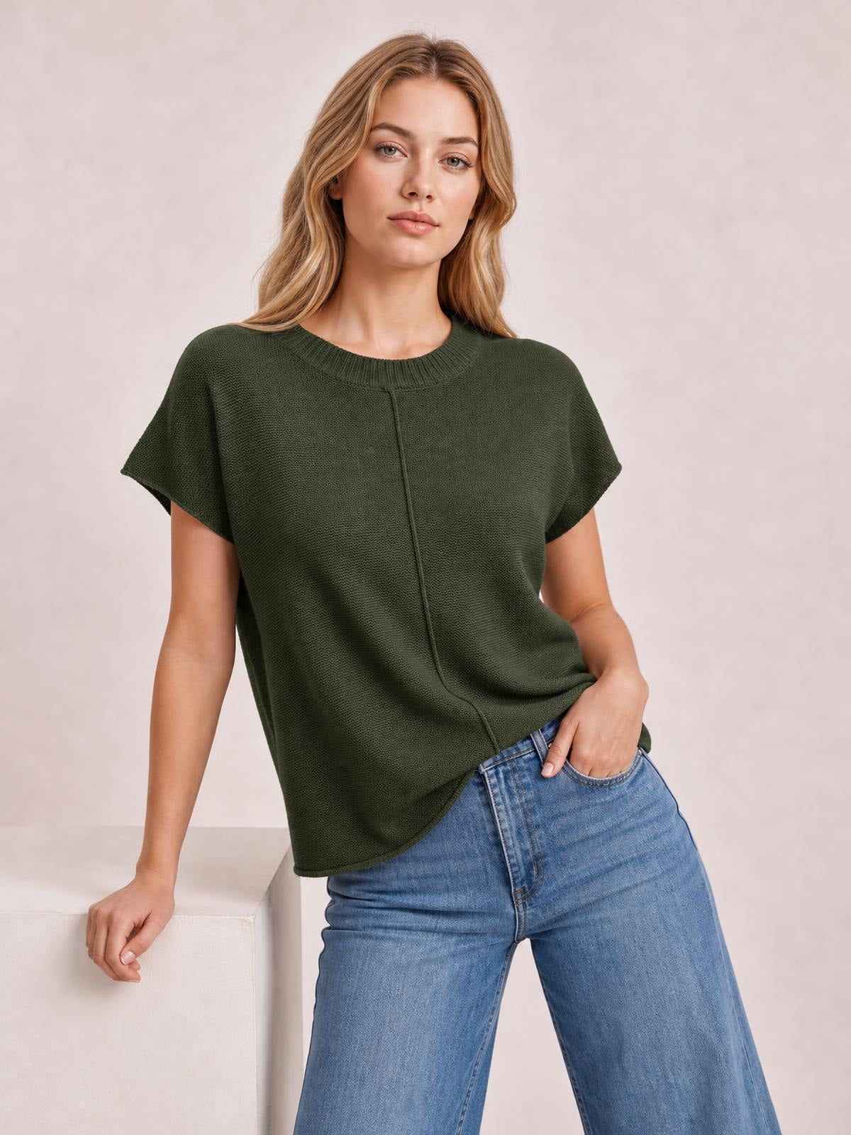 Model wearing a dark olive exposed-seam round-neck short-sleeve sweater with a relaxed, boxy silhouette and textured knit construction.