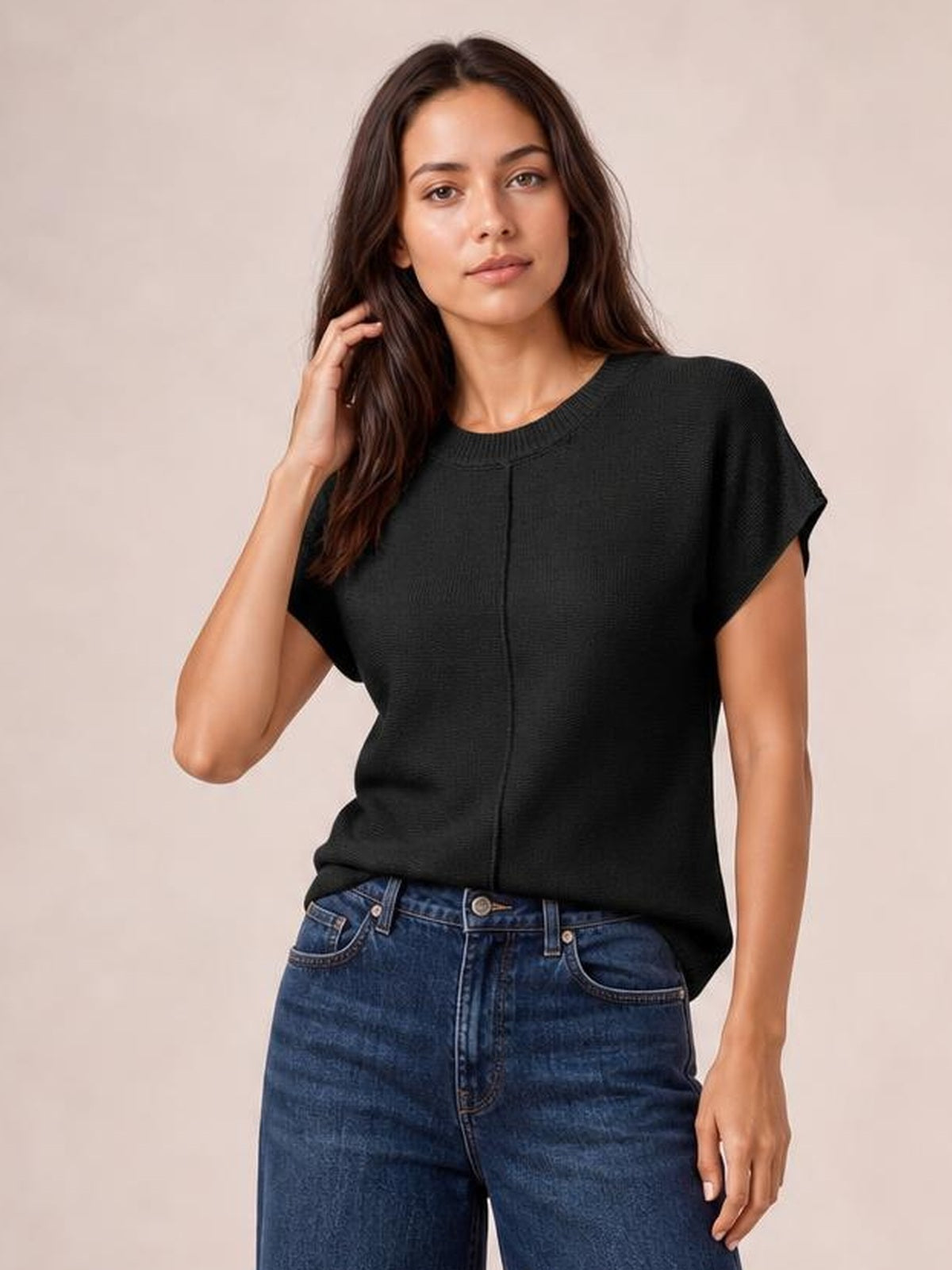 Model in a relaxed pose wears a black round neck short sleeve sweater with exposed center seam and a loose, straight silhouette.