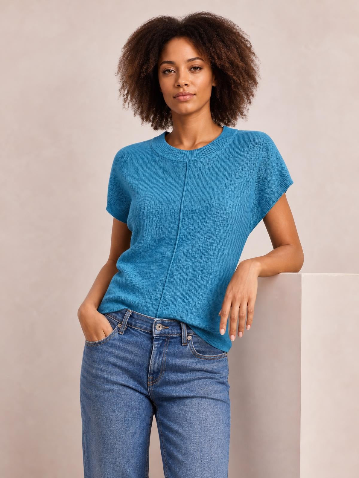 Model poses in a bright blue exposed seam round neck sweater with short sleeves, ribbed trim, and a relaxed straight silhouette.