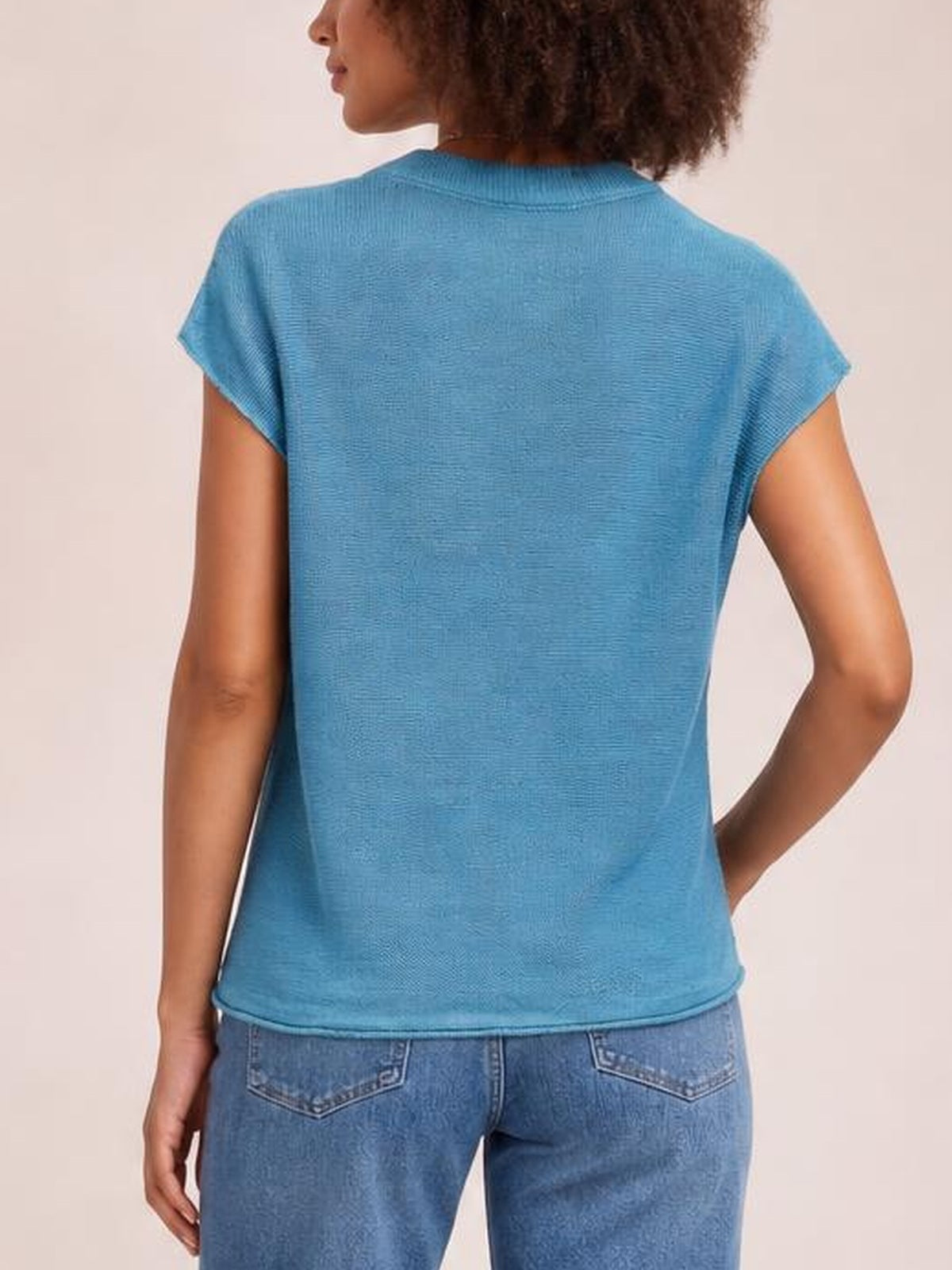 Model shown from the back wearing a blue exposed-seam round-neck short-sleeve sweater with a relaxed straight silhouette and ribbed edges.