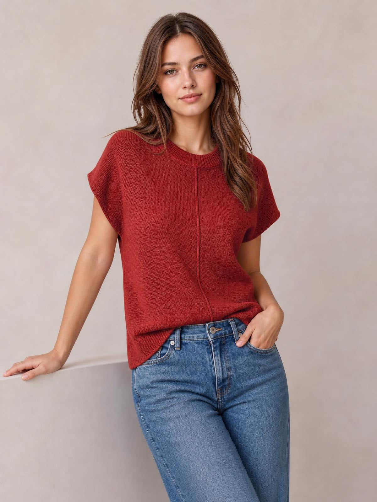 Model poses in a rust-red round neck short sleeve sweater with exposed center seam, relaxed boxy silhouette, and ribbed neckline and hem.