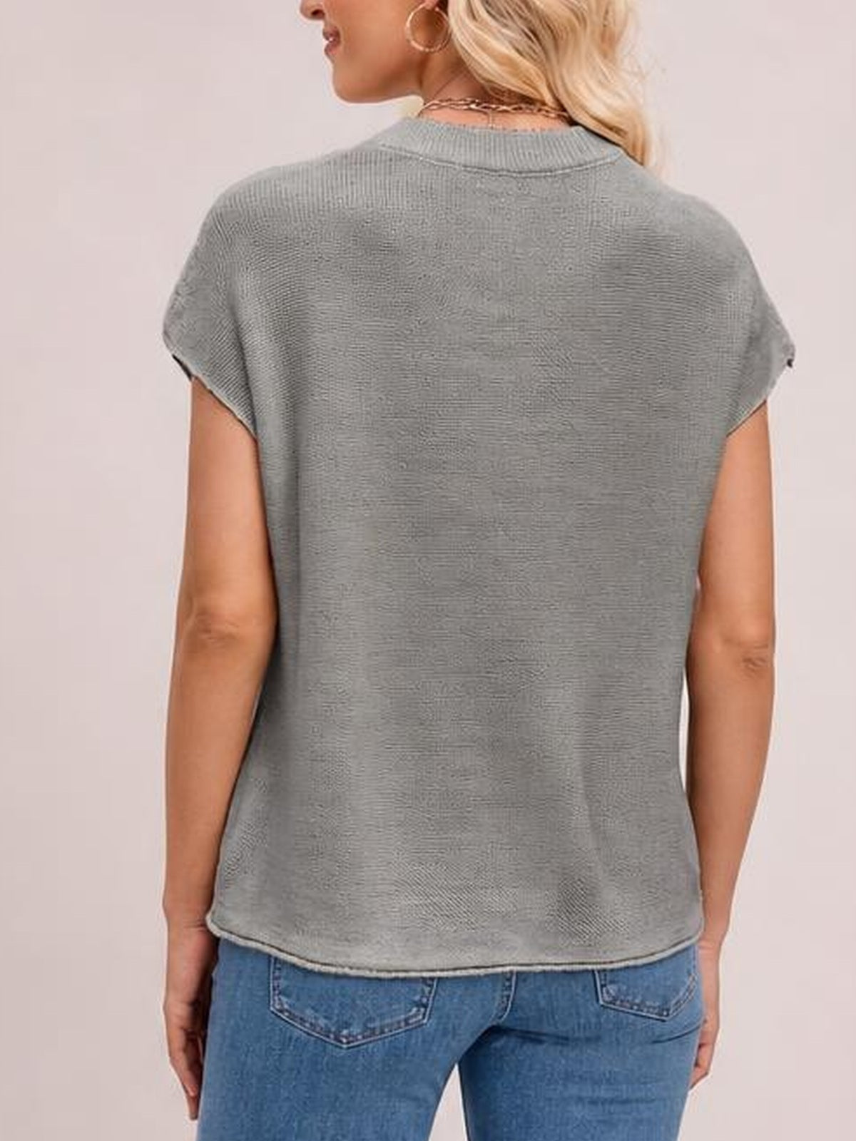 A model stands facing away in a gray exposed seam sweater with a round neck, short sleeves, relaxed silhouette, and visible ribbed neckline and hem.