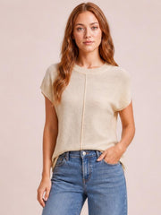 Model wearing a cream exposed seam round neck short sleeve sweater with a relaxed straight silhouette, paired with blue jeans and one hand in a pocket.