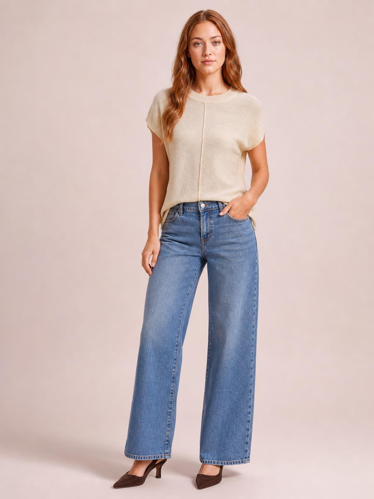 A model wears a cream exposed-seam sweater with a round neck, short sleeves, and a relaxed straight silhouette, posing with one hand in her jeans pocket.